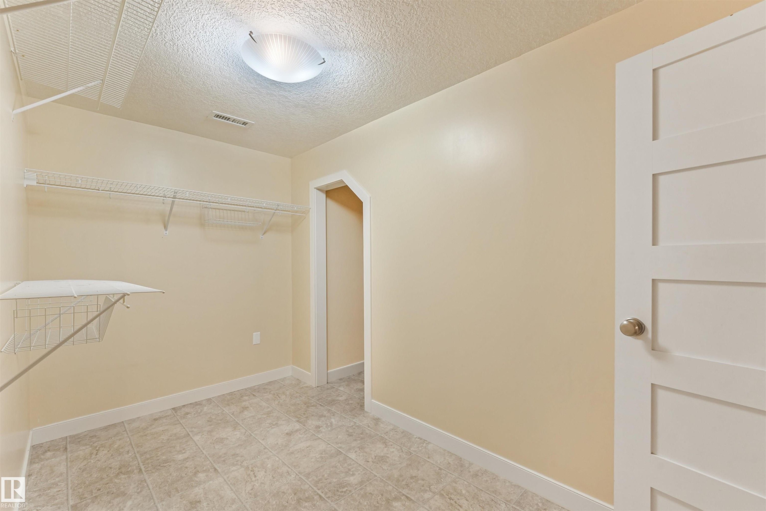 Tile flooring, wire shelving, flush mount ceiling light, paneled interior door, and neutral wall paint - 8212 148 Street Nw, Edmonton, AB