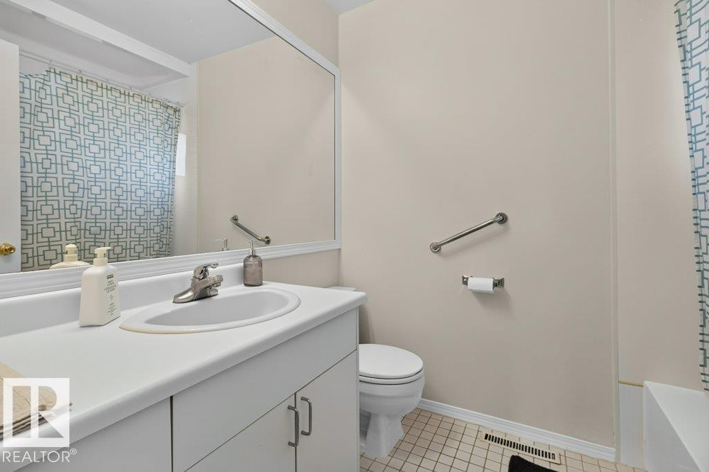 Bathroom featuring a vanity with an integrated sink, a large wall-mounted mirror, a toilet, and a bathtub with grab bar - #74 22555 Twp Road 530, Rural Strathcona County, AB