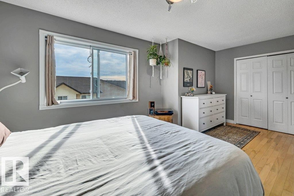 Hardwood-style flooring, white paneled bi-fold closet doors, and large window with white trim - #24 3811 85 St Nw, Edmonton, AB