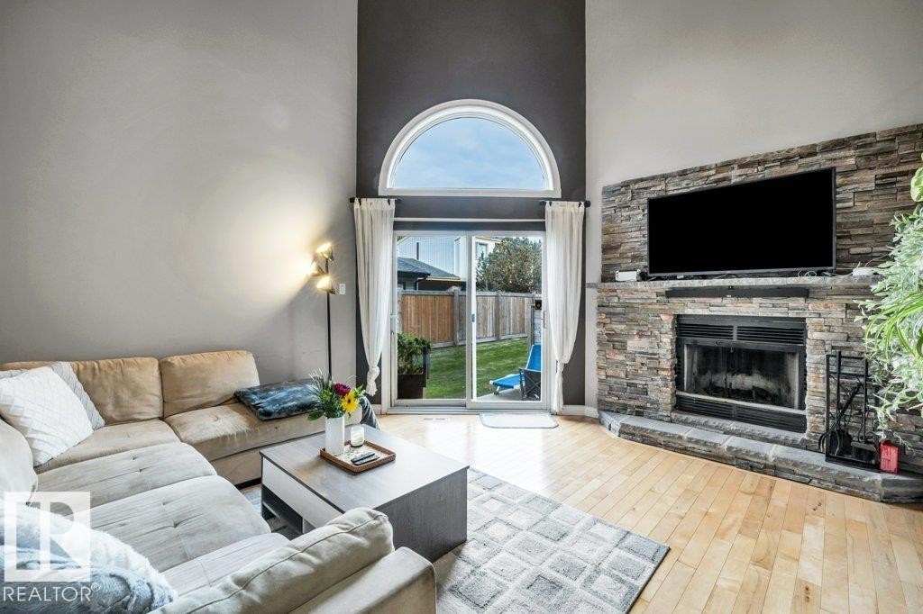Vaulted ceiling, stone-clad fireplace, wood-finish flooring, sliding glass door, and an arched transom window - #24 3811 85 St Nw, Edmonton, AB