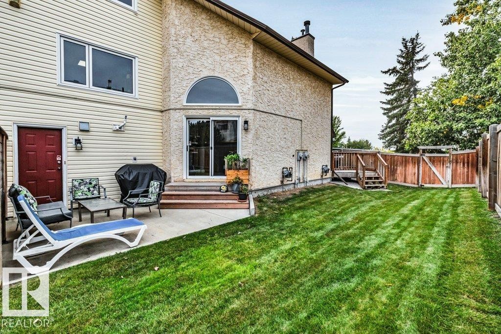 Expansive green lawn, concrete patio, wood fencing, exterior siding, and a rear deck with stairs - #24 3811 85 St Nw, Edmonton, AB