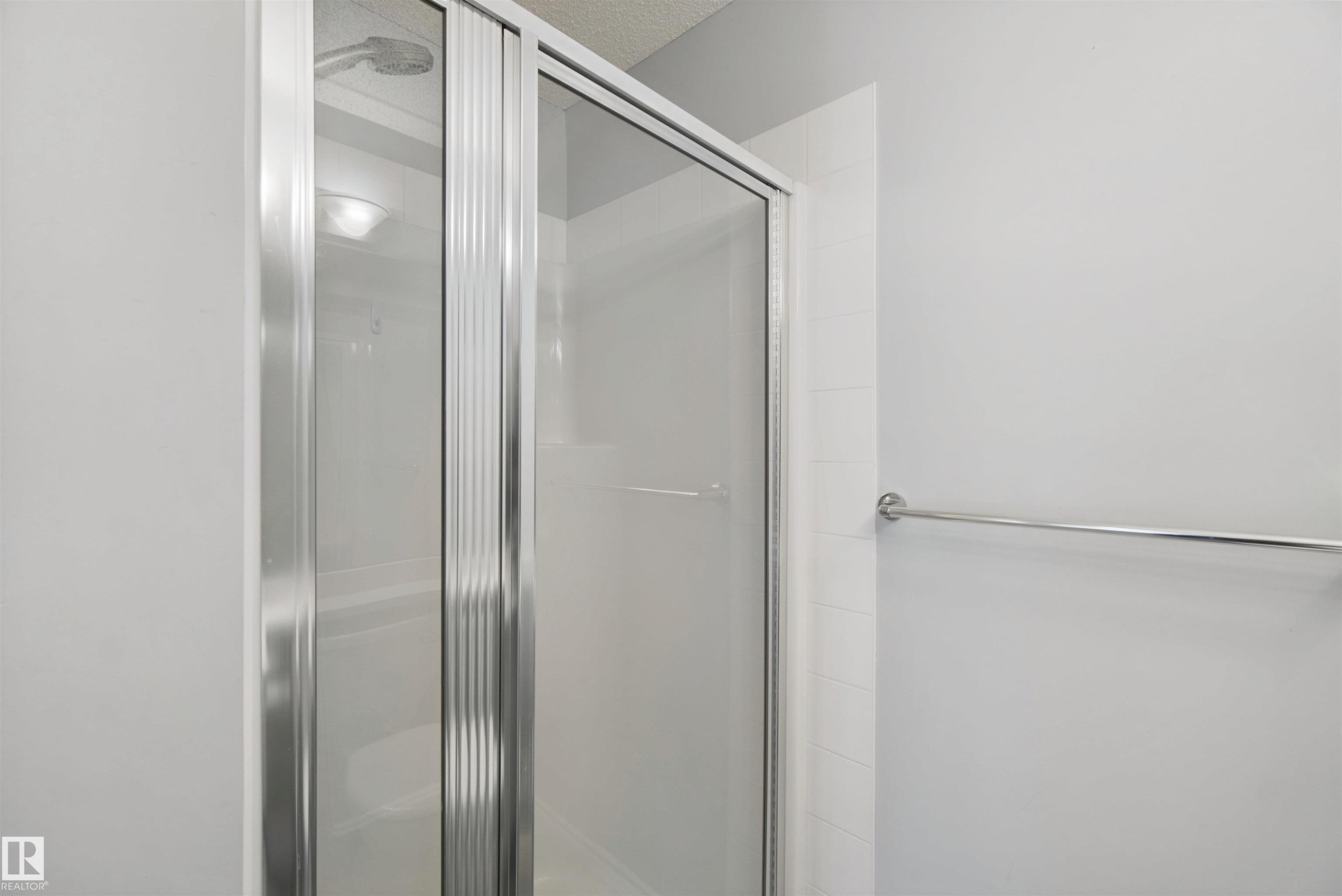 Shower enclosure with sliding glass doors, chrome hardware, and a white tiled surround - #208 16035 132 St Nw, Edmonton, AB