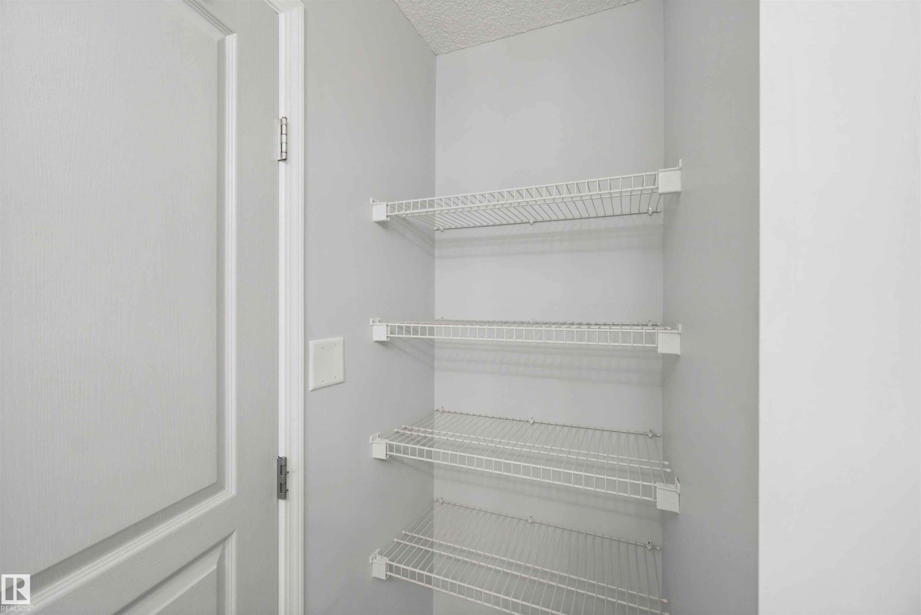 Built-in wire shelving within a storage closet, featuring light gray wall paint and white trim details - #208 16035 132 St Nw, Edmonton, AB
