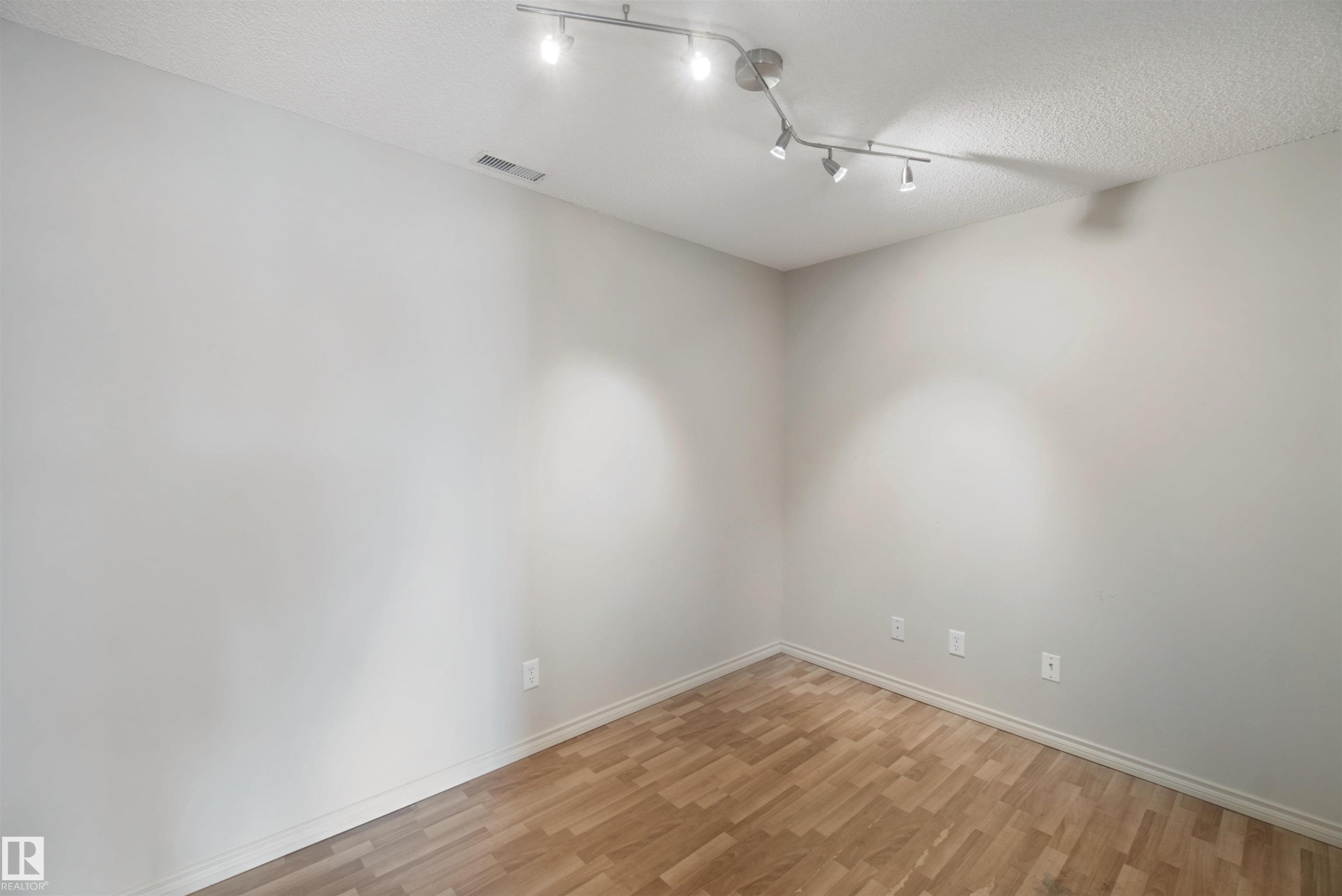 Recessed light fixture with track lighting, textured ceiling, light-toned walls, and wood-finish flooring - #208 16035 132 St Nw, Edmonton, AB