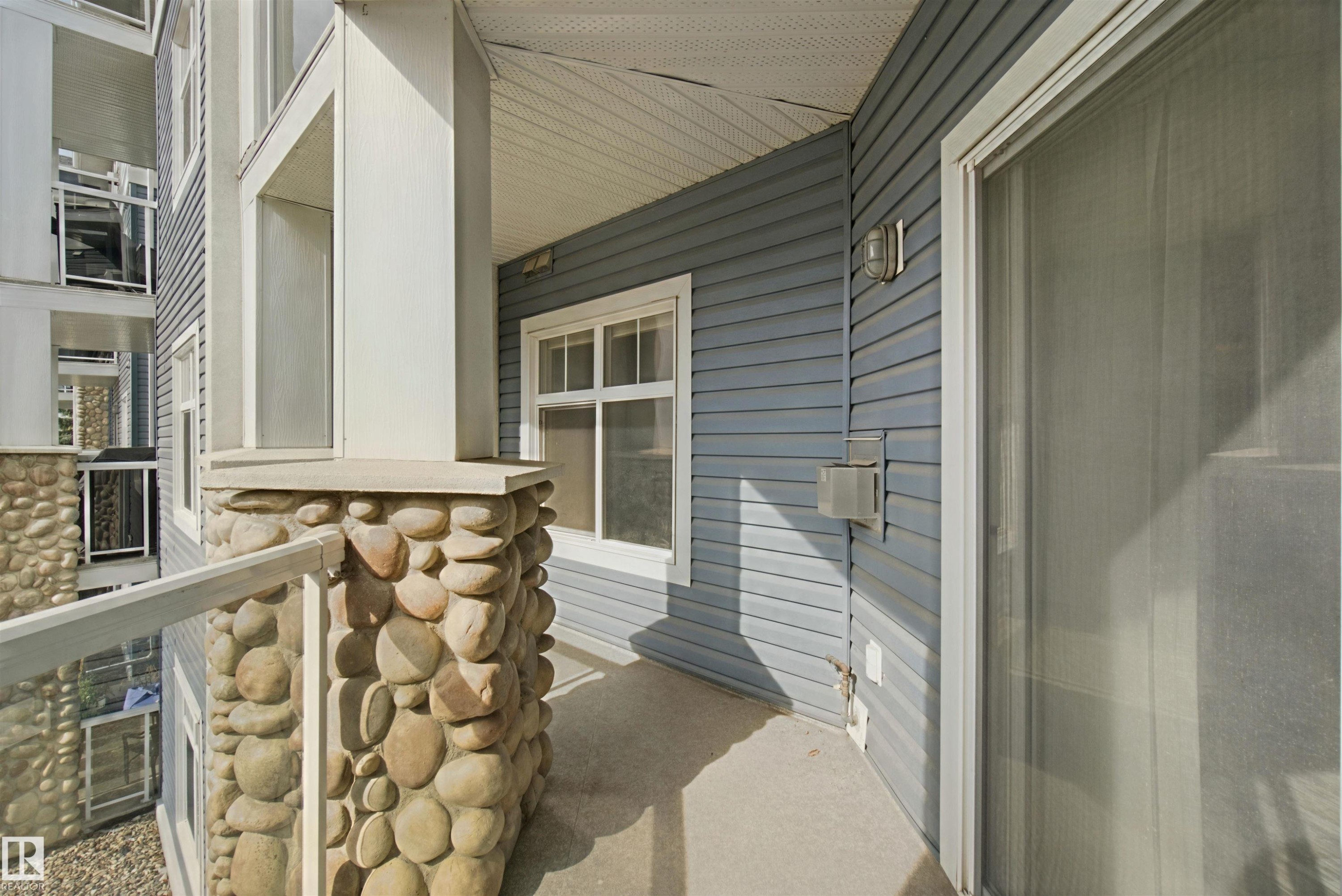Balcony with river rock column, glass railing, concrete flooring, and sliding glass door access - #208 16035 132 St Nw, Edmonton, AB