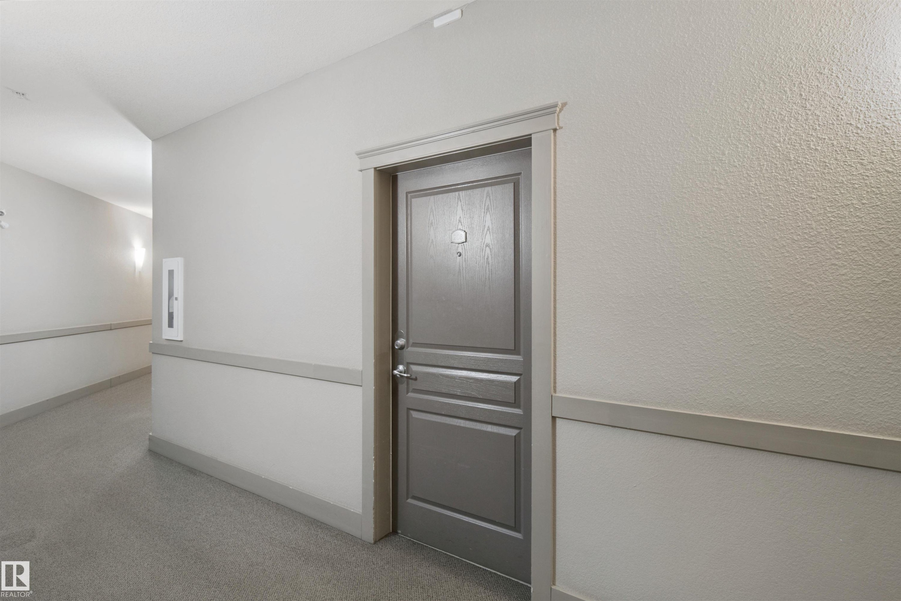 Textured wall finish, panel door with hardware, wall-mounted light fixture, fire extinguisher cabinet, and baseboard trim - #208 16035 132 St Nw, Edmonton, AB