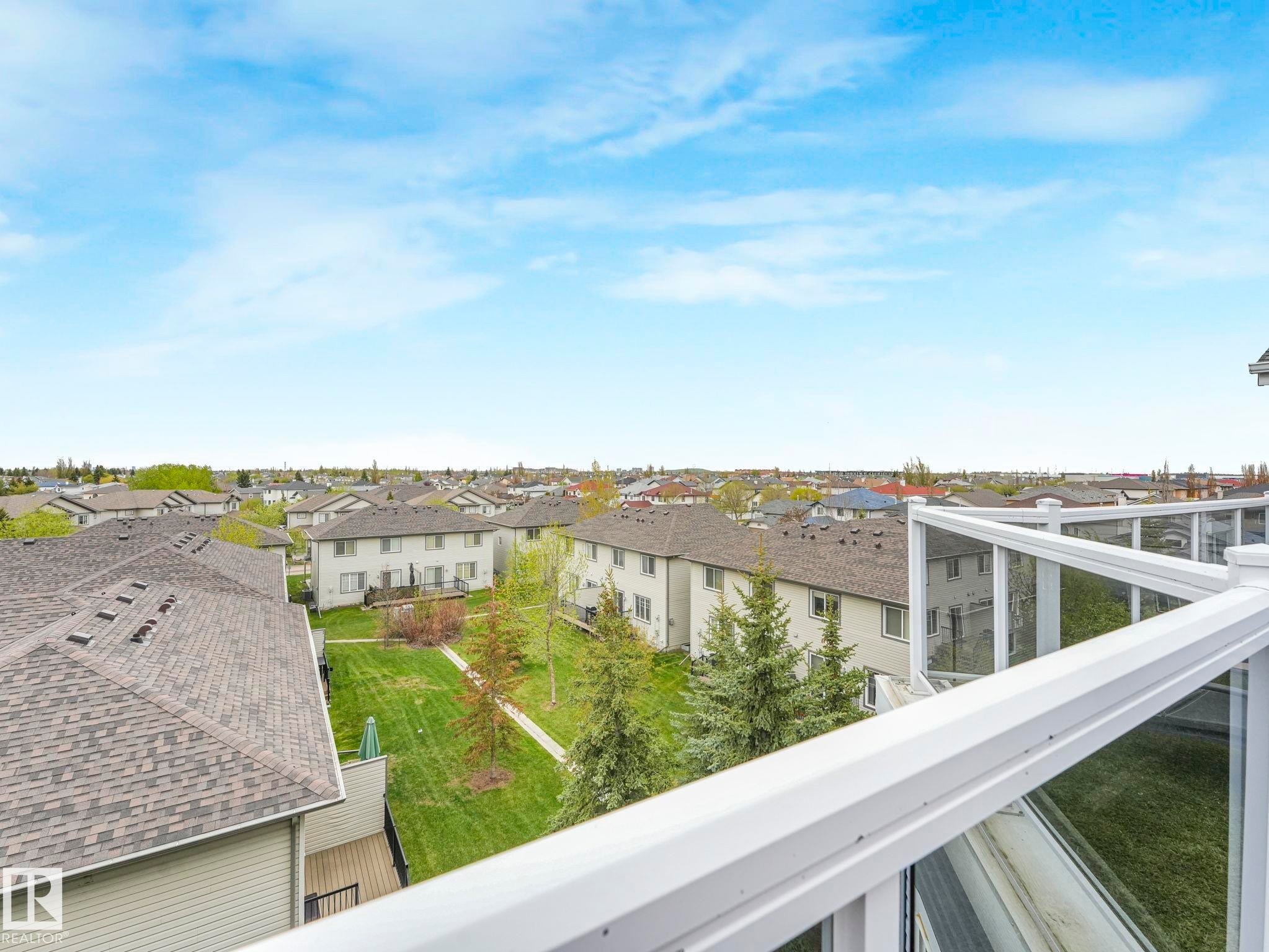 White railing with glass panels overlooking residential neighborhood roofs and green spaces - #208 16035 132 St Nw, Edmonton, AB