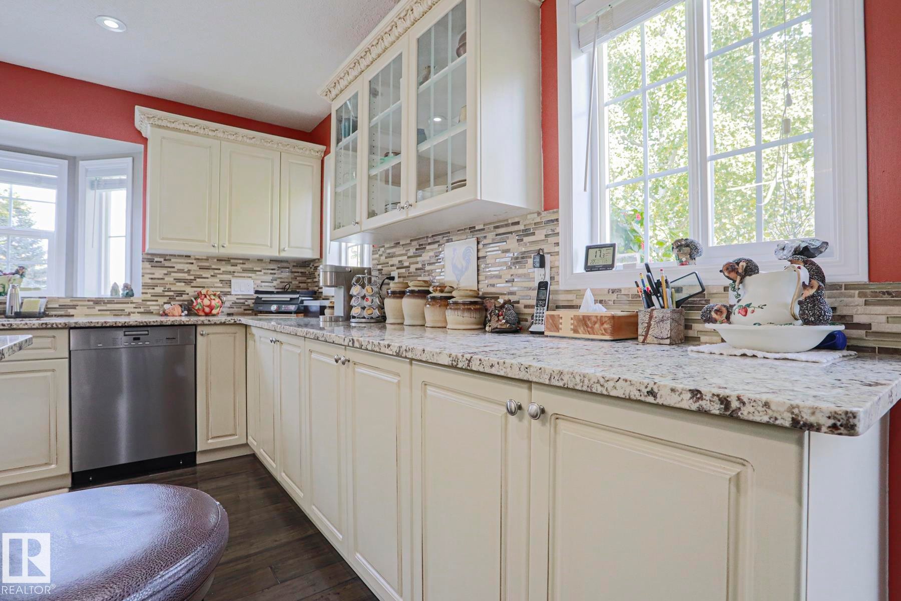 Cream-colored cabinetry with decorative crown molding, stainless steel dishwasher, speckled countertops, and a mosaic tile backsplash - 3815 41 Street Nw, Edmonton, AB