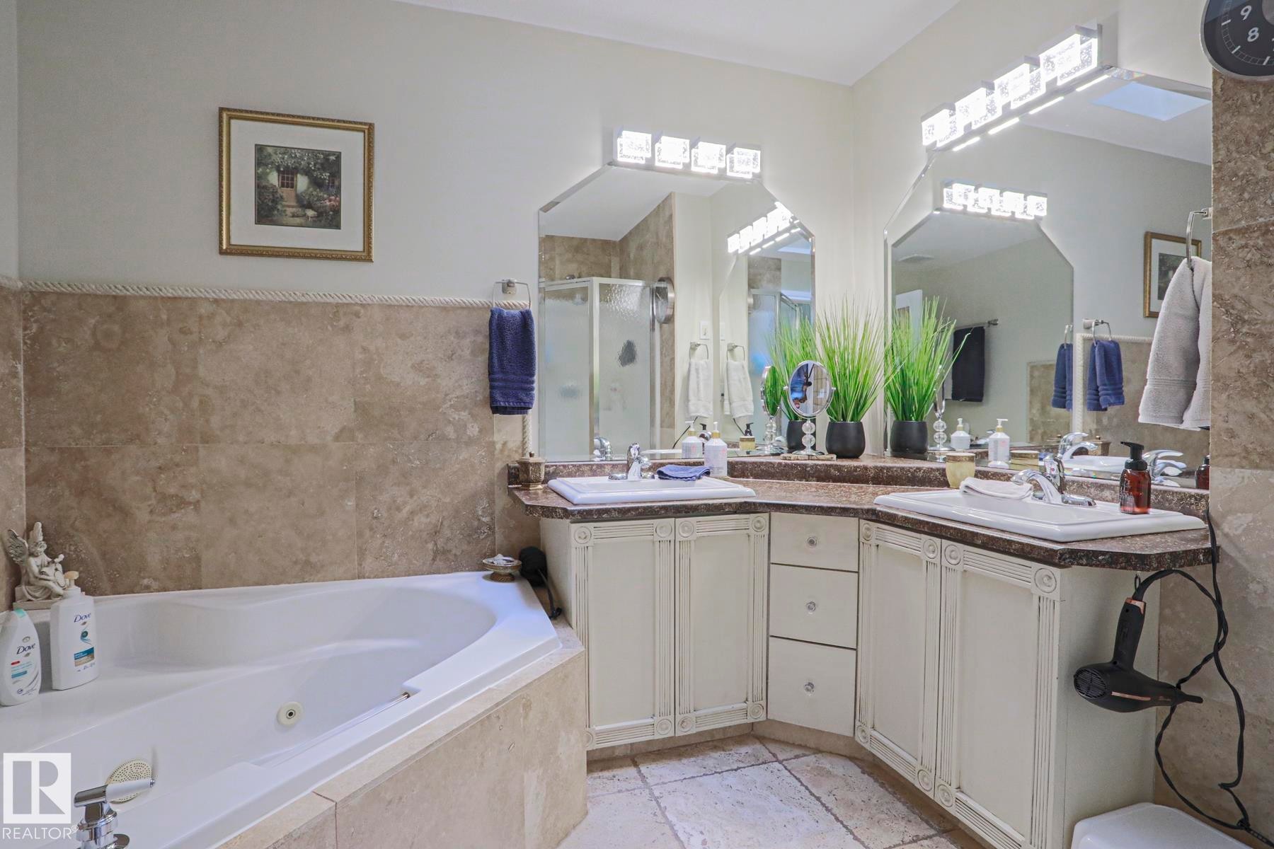 Corner soaking tub, dual vanity with integrated sinks, framed mirrors, stone tile walls, and a separate shower enclosure - 3815 41 Street Nw, Edmonton, AB