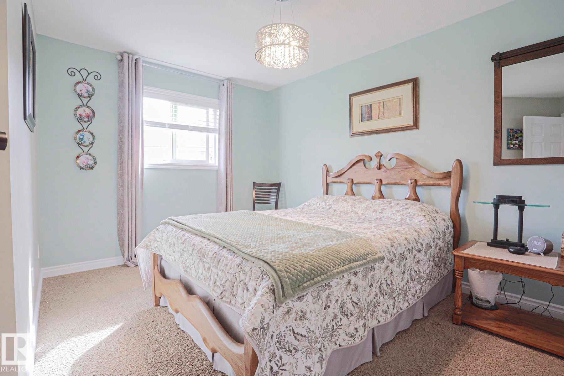 Wall-to-wall carpeting, wood bed frame, wood-framed mirror, and a decorative ceiling light fixture - 3815 41 Street Nw, Edmonton, AB