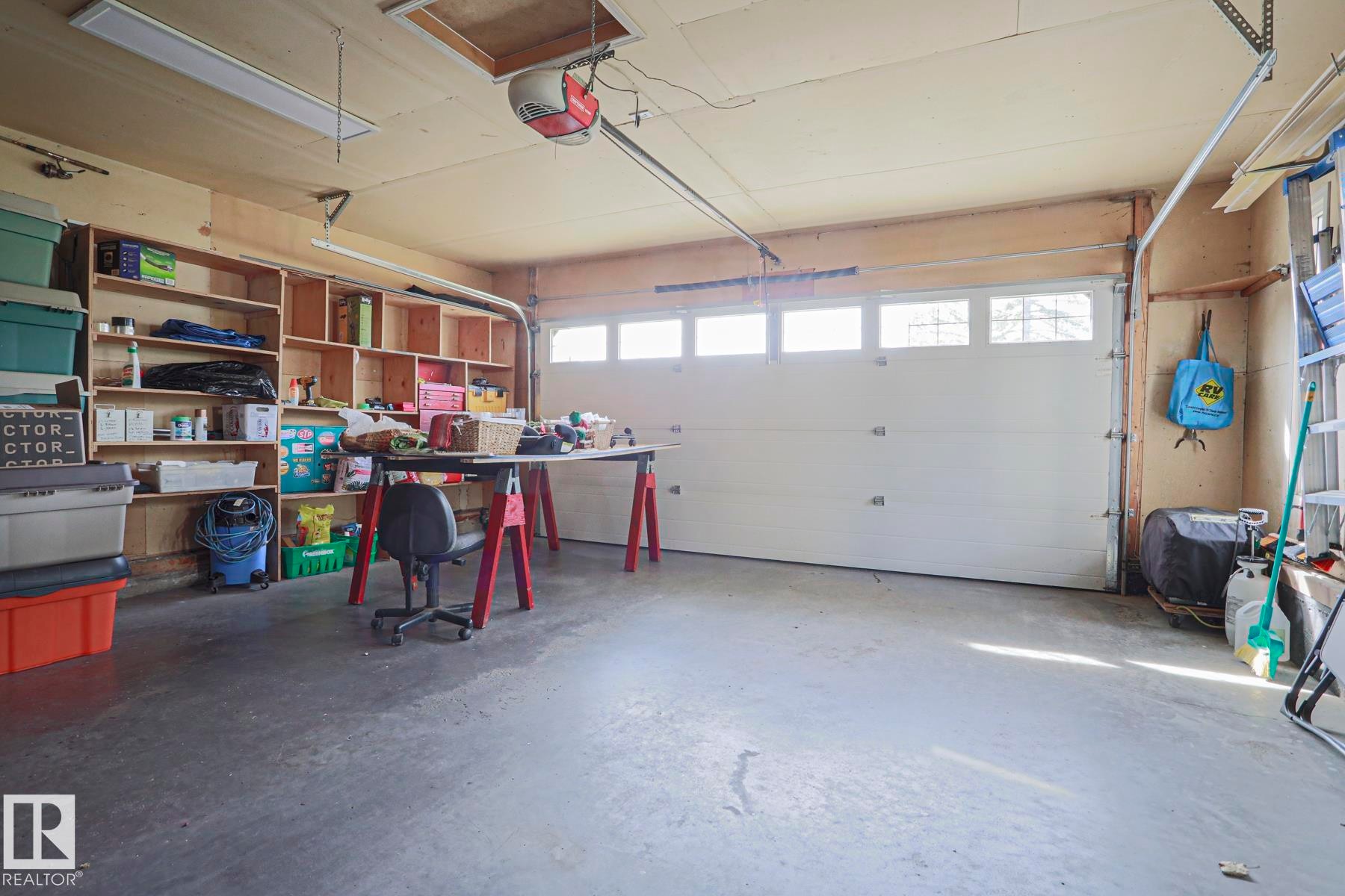 Spacious garage with built-in wooden shelving, a white paneled garage door with windows, concrete flooring, and overhead fluorescent lighting - 3815 41 Street Nw, Edmonton, AB
