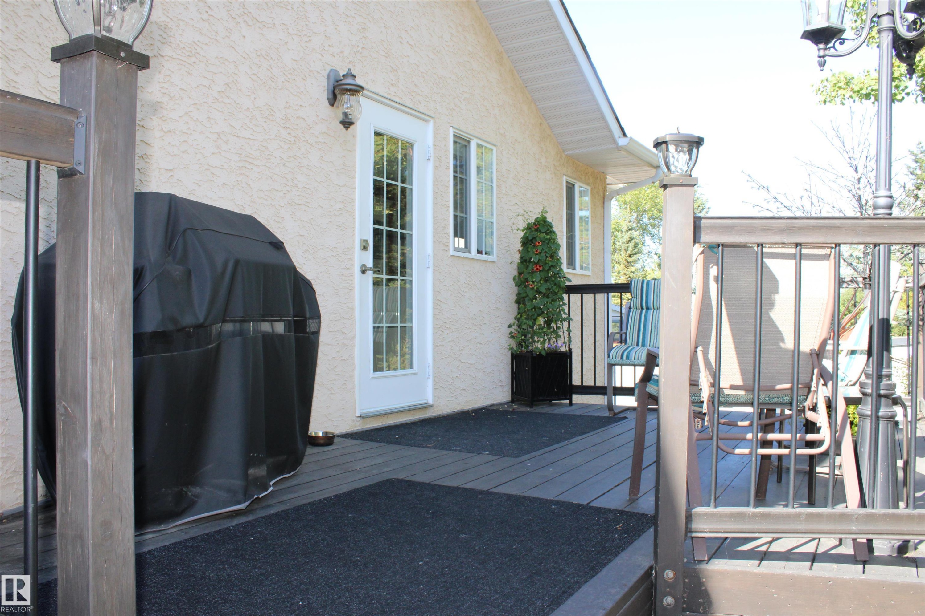 Deck with composite decking, decorative metal railing, a side entry door with window panes, and an exterior wall light fixture - 3815 41 Street Nw, Edmonton, AB