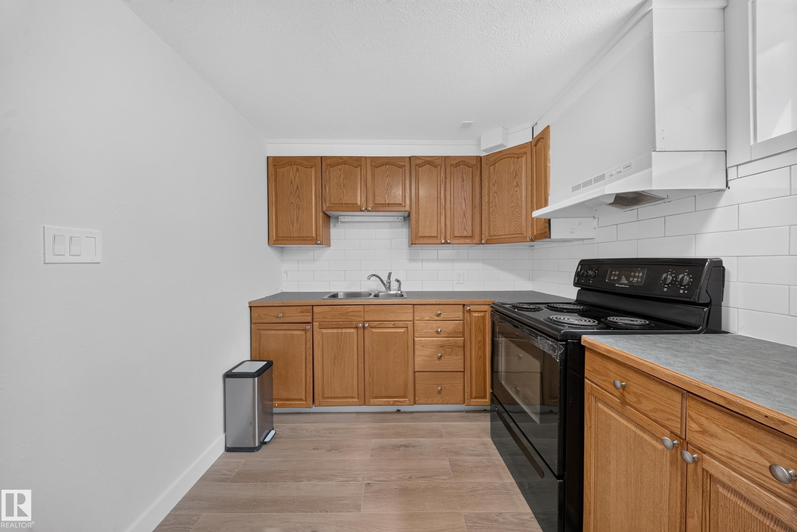 Kitchen with wood cabinetry, white subway tile backsplash, and wood-finish flooring - 5204 97A Avenue Nw, Edmonton, AB