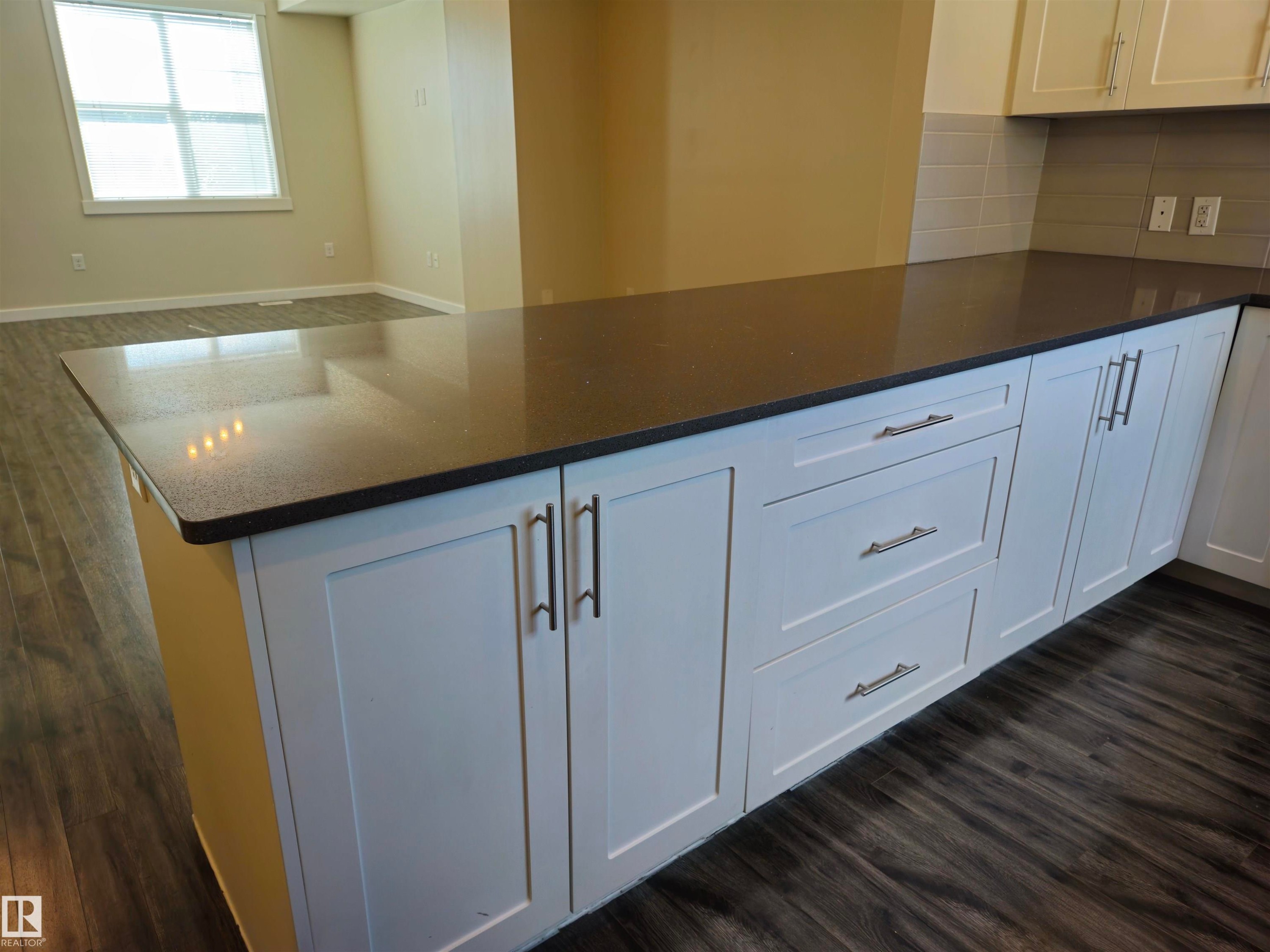 Kitchen island with a dark countertop and white shaker-style cabinetry, complemented by dark wood-finish flooring - #69 903 Crystallina Nera Wy Nw, Edmonton, AB
