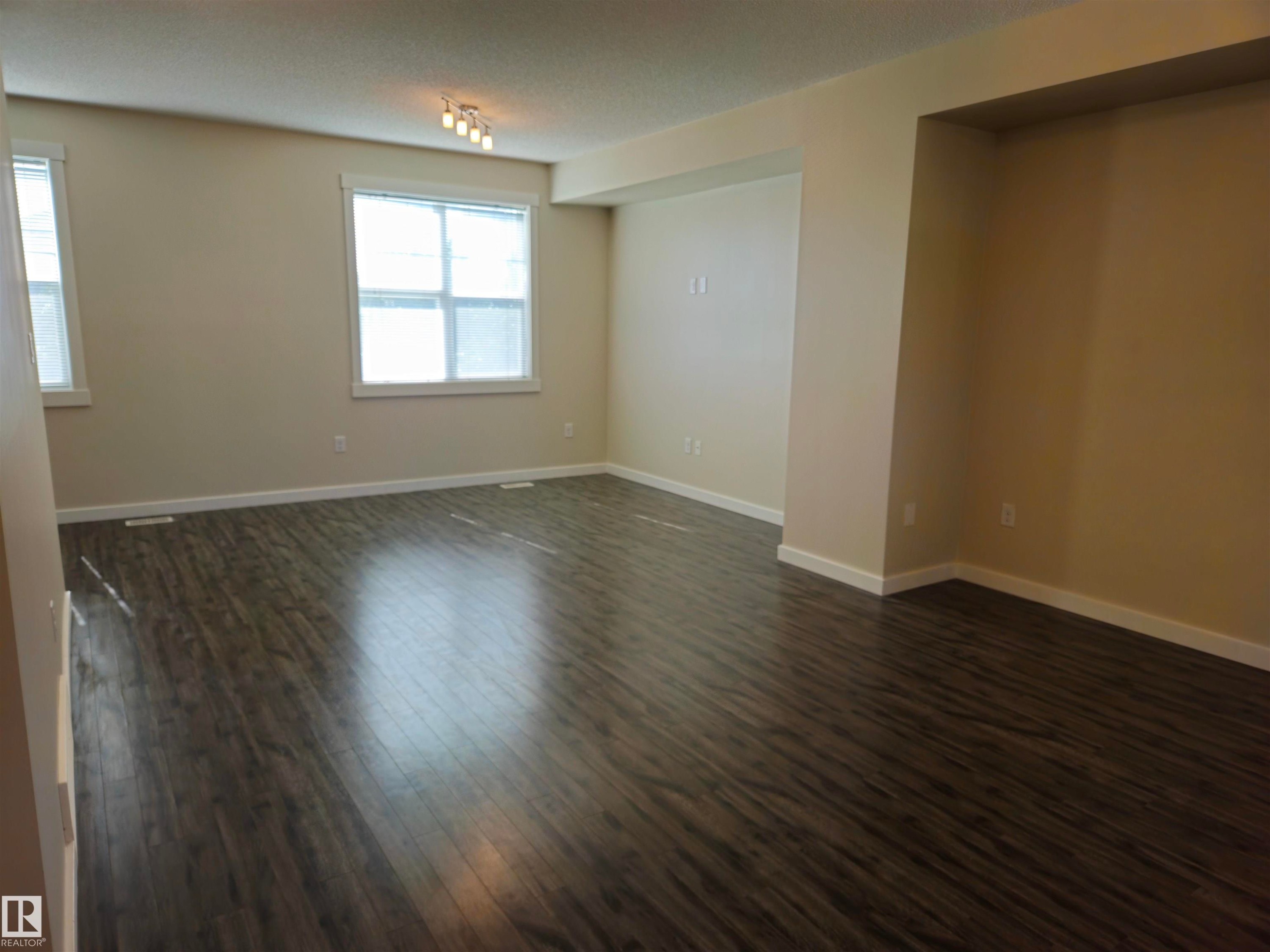 Room featuring wood-finish flooring, multiple windows with white trim, recessed wall alcove, and neutral wall paint - #69 903 Crystallina Nera Wy Nw, Edmonton, AB