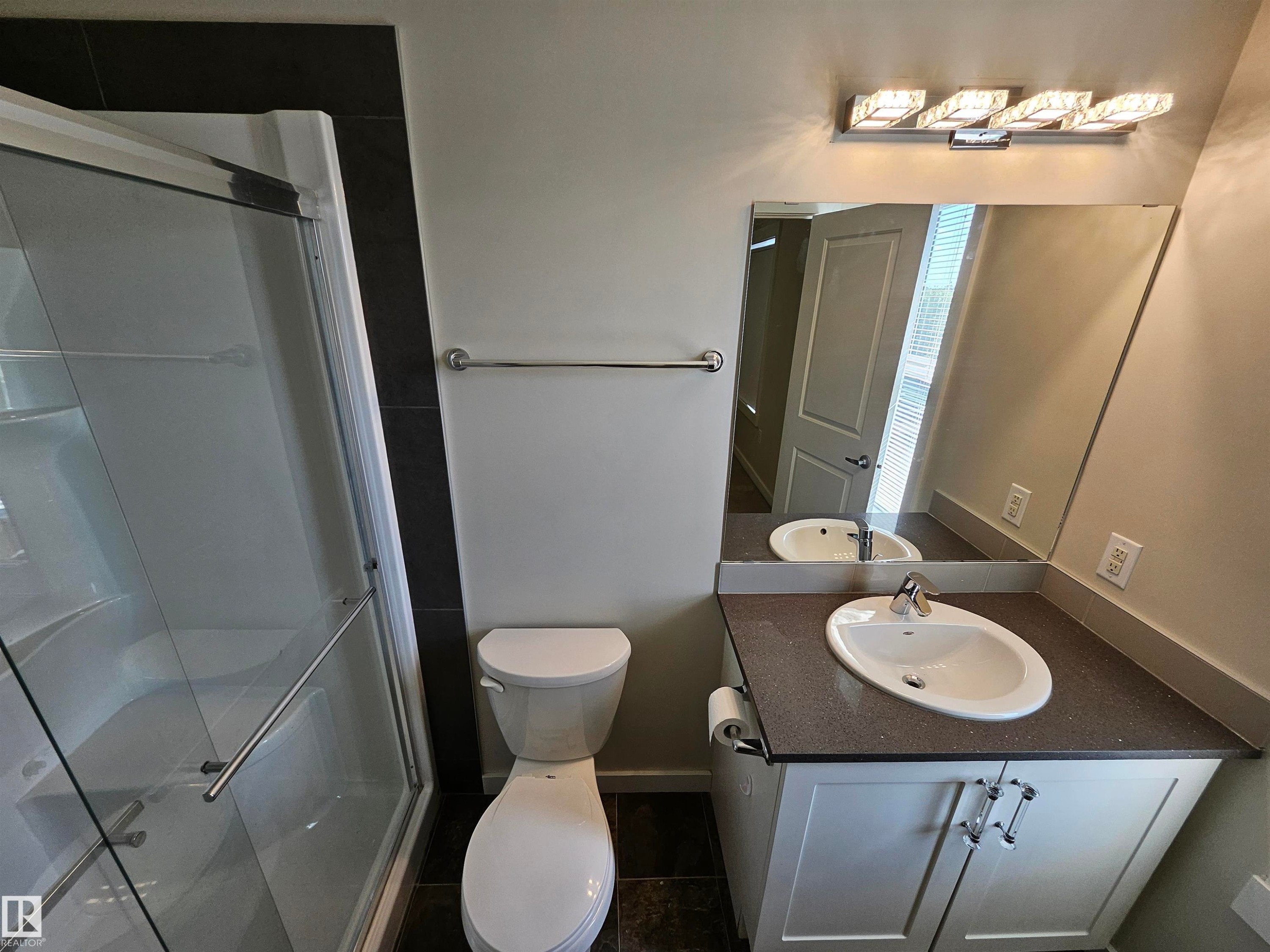 Shower enclosure with glass door, vanity with integrated sink, rectangular mirror, and wall-mounted light fixture - #69 903 Crystallina Nera Wy Nw, Edmonton, AB