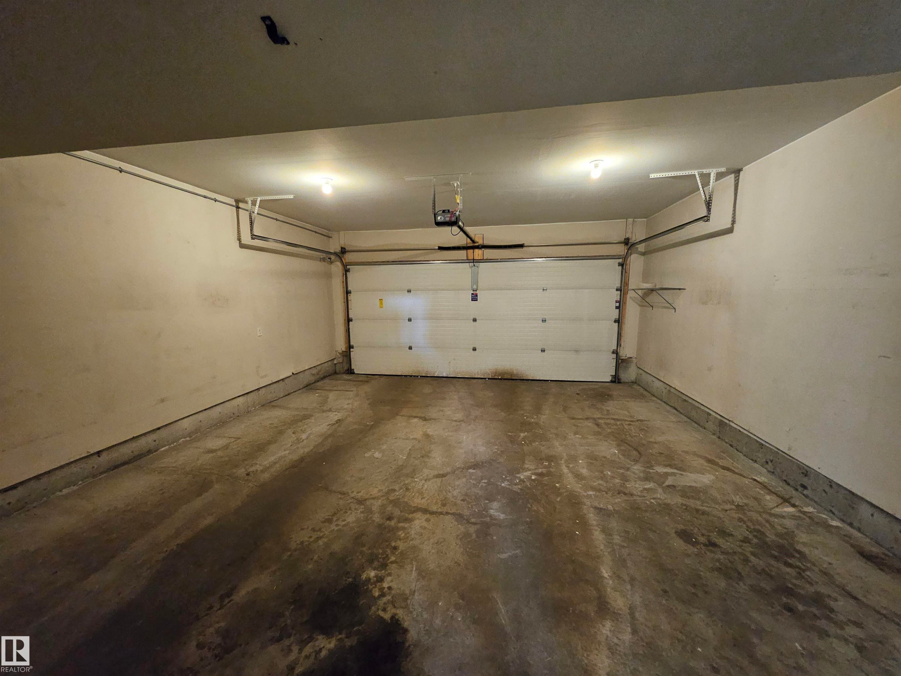 Enclosed garage featuring a concrete floor, overhead lighting, and built-in shelving - #69 903 Crystallina Nera Wy Nw, Edmonton, AB