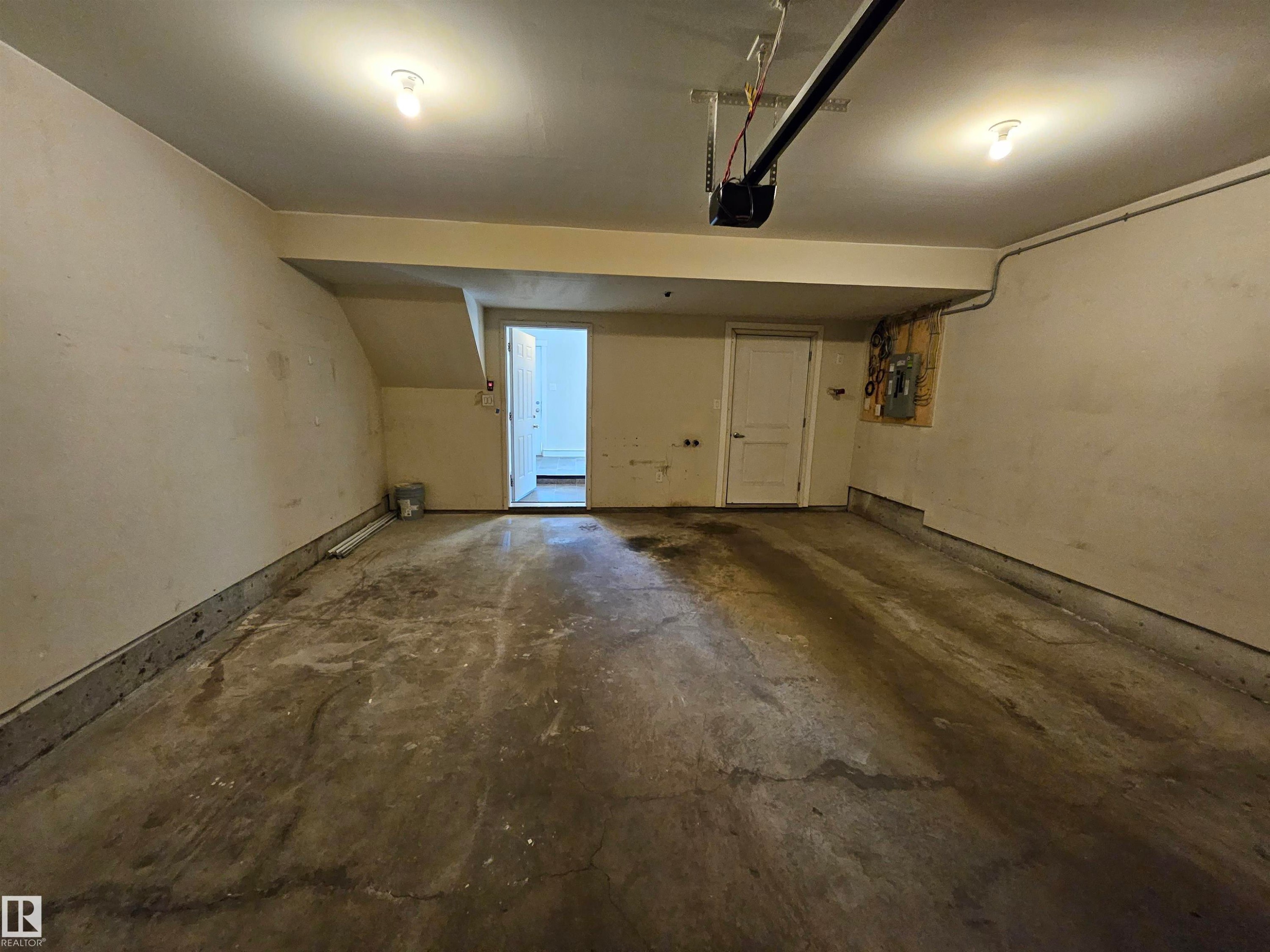 Concrete flooring garage with an automatic garage door opener, two overhead light fixtures, and two entry doors - #69 903 Crystallina Nera Wy Nw, Edmonton, AB