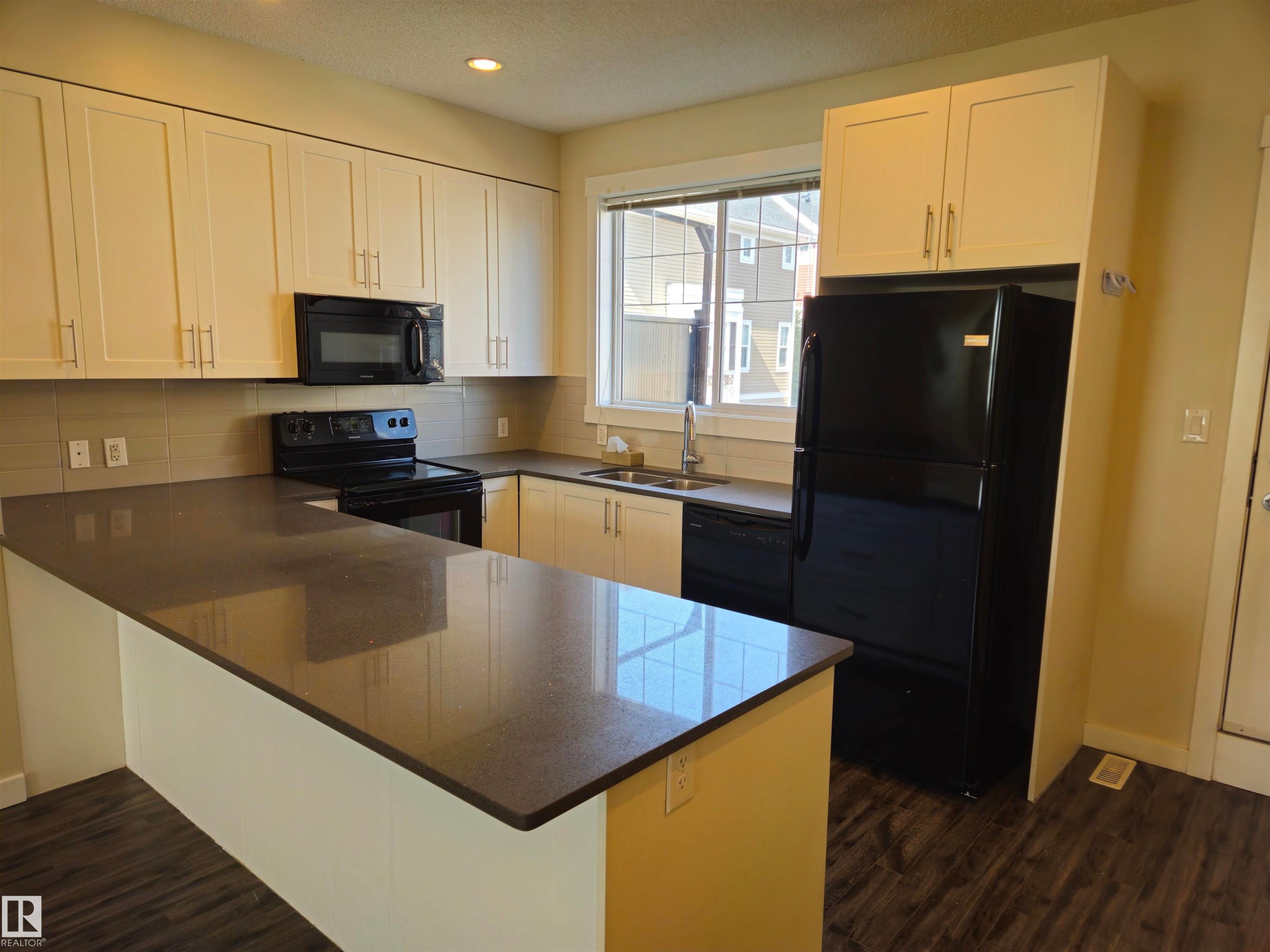 U-shaped kitchen featuring white cabinetry, dark stone countertops, a tile backsplash, stainless steel sink, and wood-finish flooring - #69 903 Crystallina Nera Wy Nw, Edmonton, AB