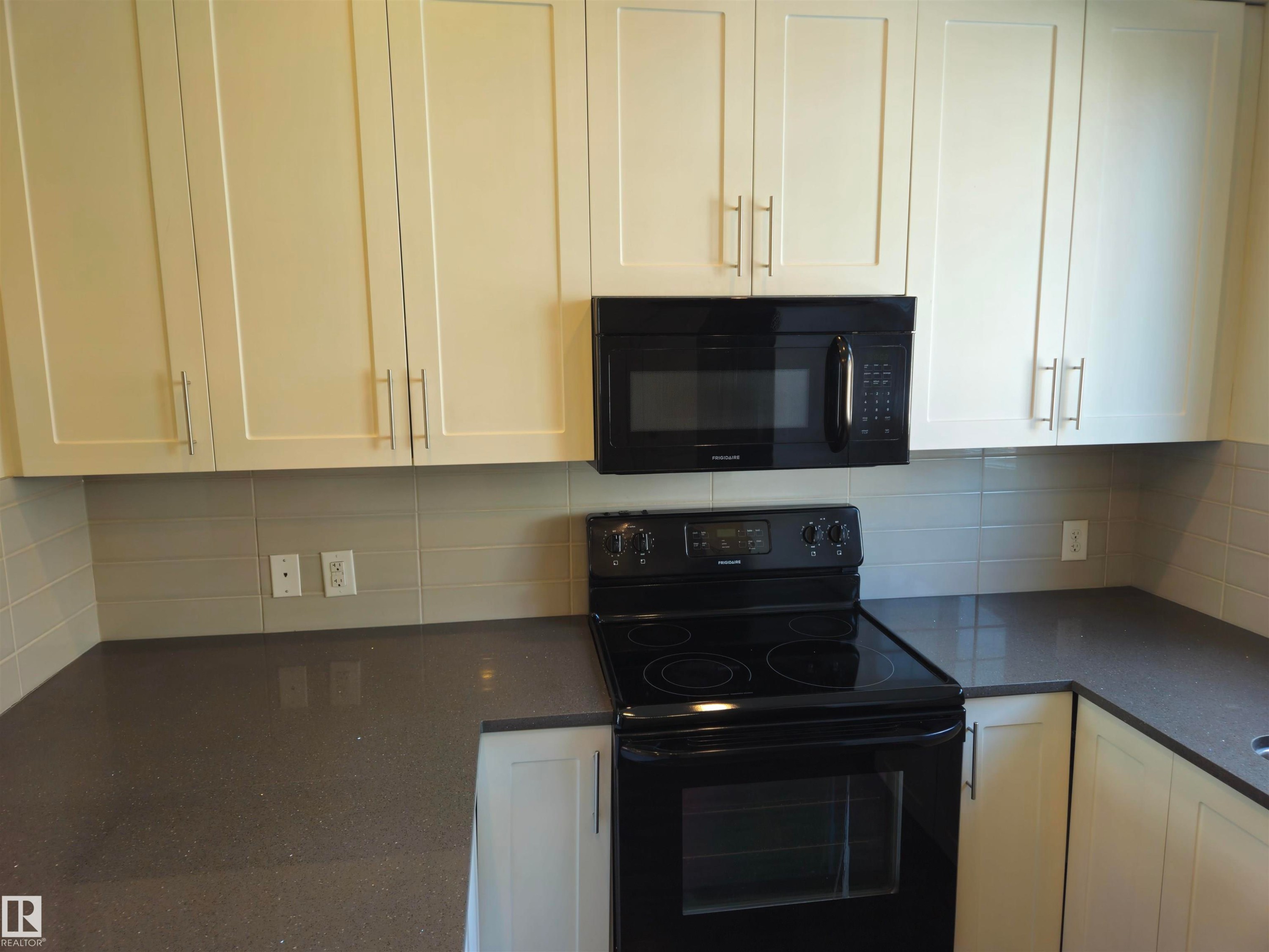 Modern kitchen featuring cream shaker-style cabinetry, dark speckled countertops, a grey subway tile backsplash, and black appliances - #69 903 Crystallina Nera Wy Nw, Edmonton, AB