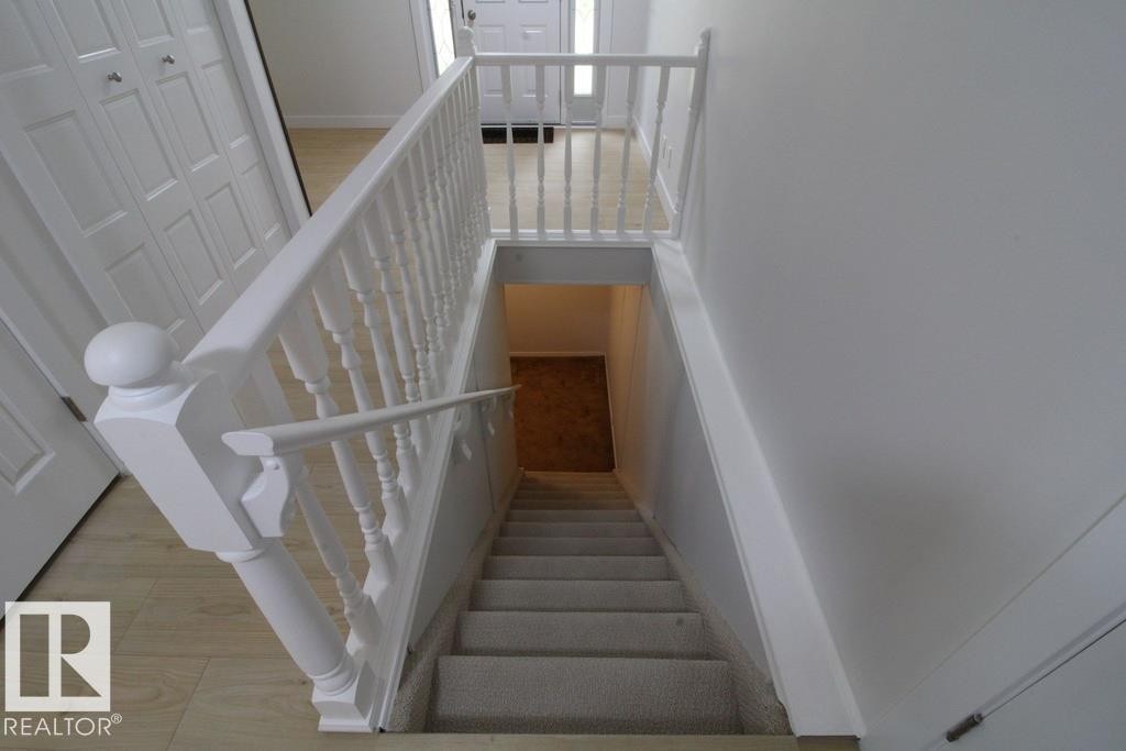 Light wood-finish flooring, white paneled bi-fold doors, painted white balusters, and carpeted stairs - 44 Arlington Drive, St. Albert, AB