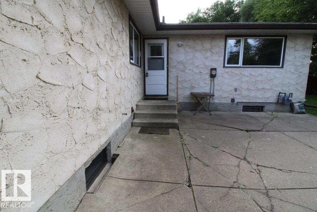 Exterior featuring textured stucco siding, white-framed windows, a white entry door, and a concrete patio - 44 Arlington Drive, St. Albert, AB