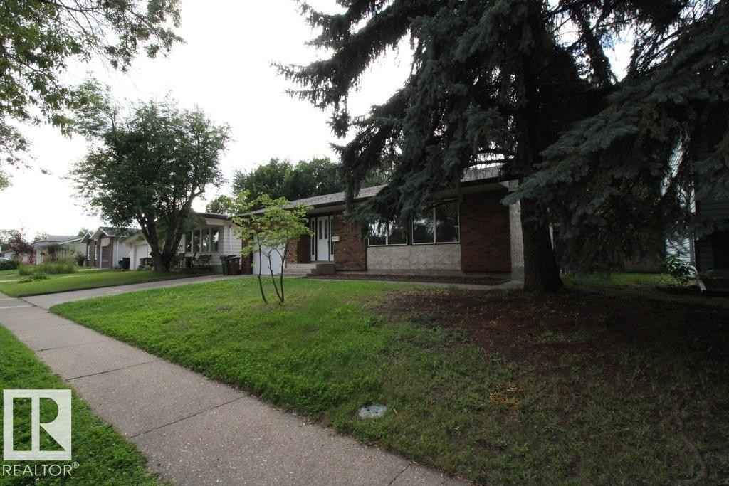 Brick and stone facade with large windows, mature trees, and a concrete pathway - 44 Arlington Drive, St. Albert, AB