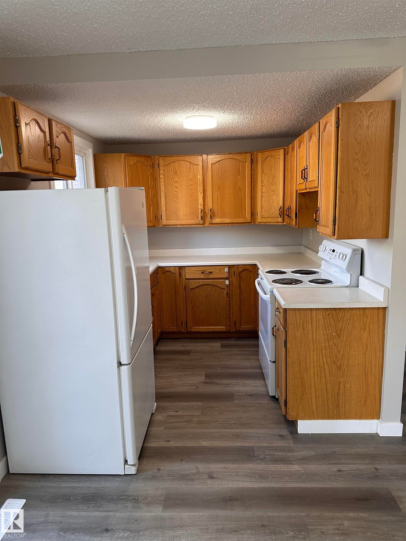 U-shaped kitchen featuring wood cabinetry, white countertops, and wood-finish flooring - 9G Clareview Village Nw, Edmonton, AB
