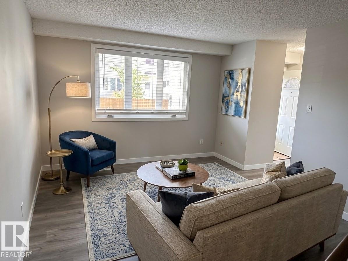 Wood-finish flooring throughout, complemented by a large window with blinds and white trim - 9G Clareview Village Nw, Edmonton, AB