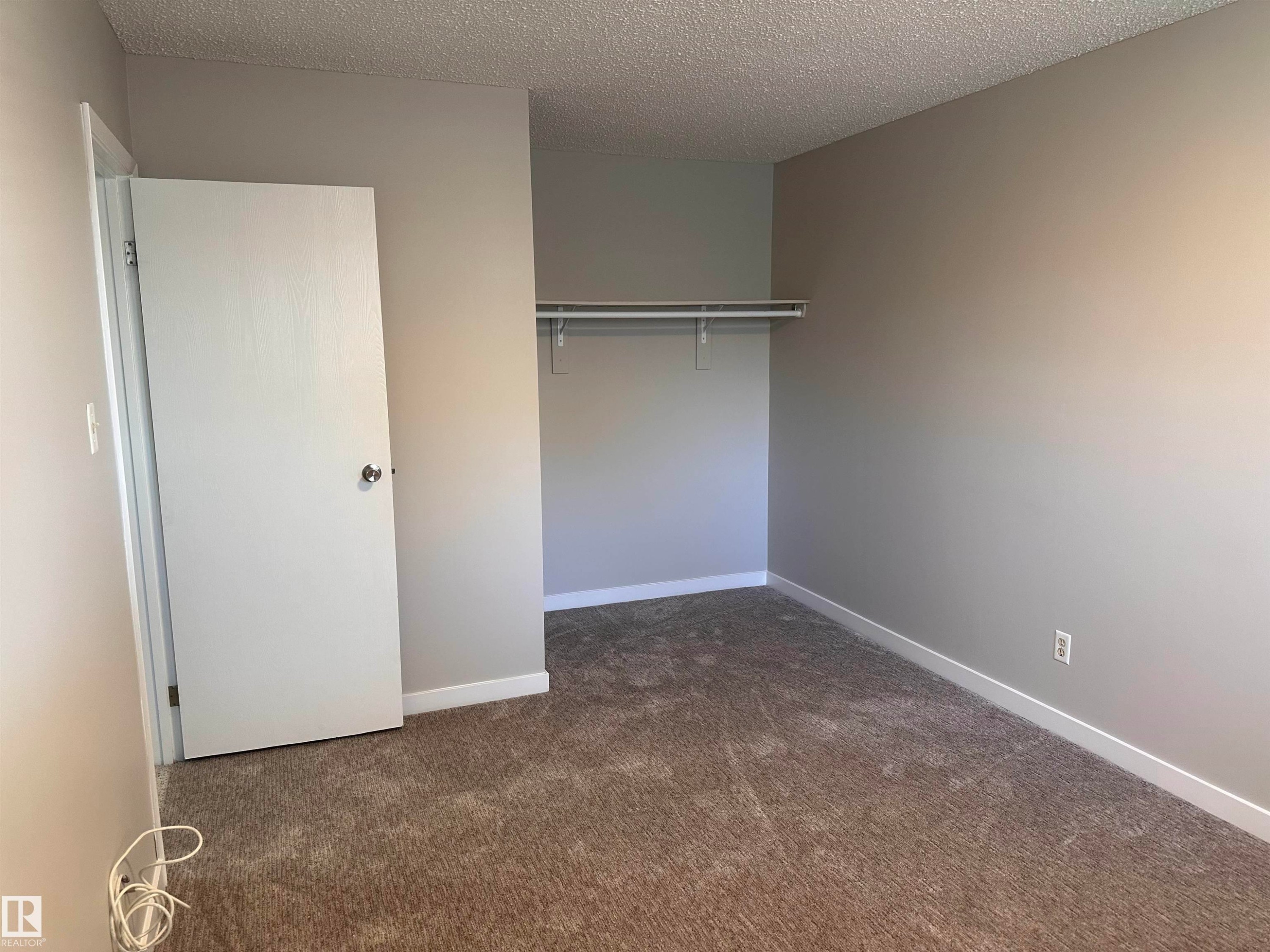 Neutral-toned walls, textured ceiling, brown carpet flooring, and a built-in closet rod - 9G Clareview Village Nw, Edmonton, AB