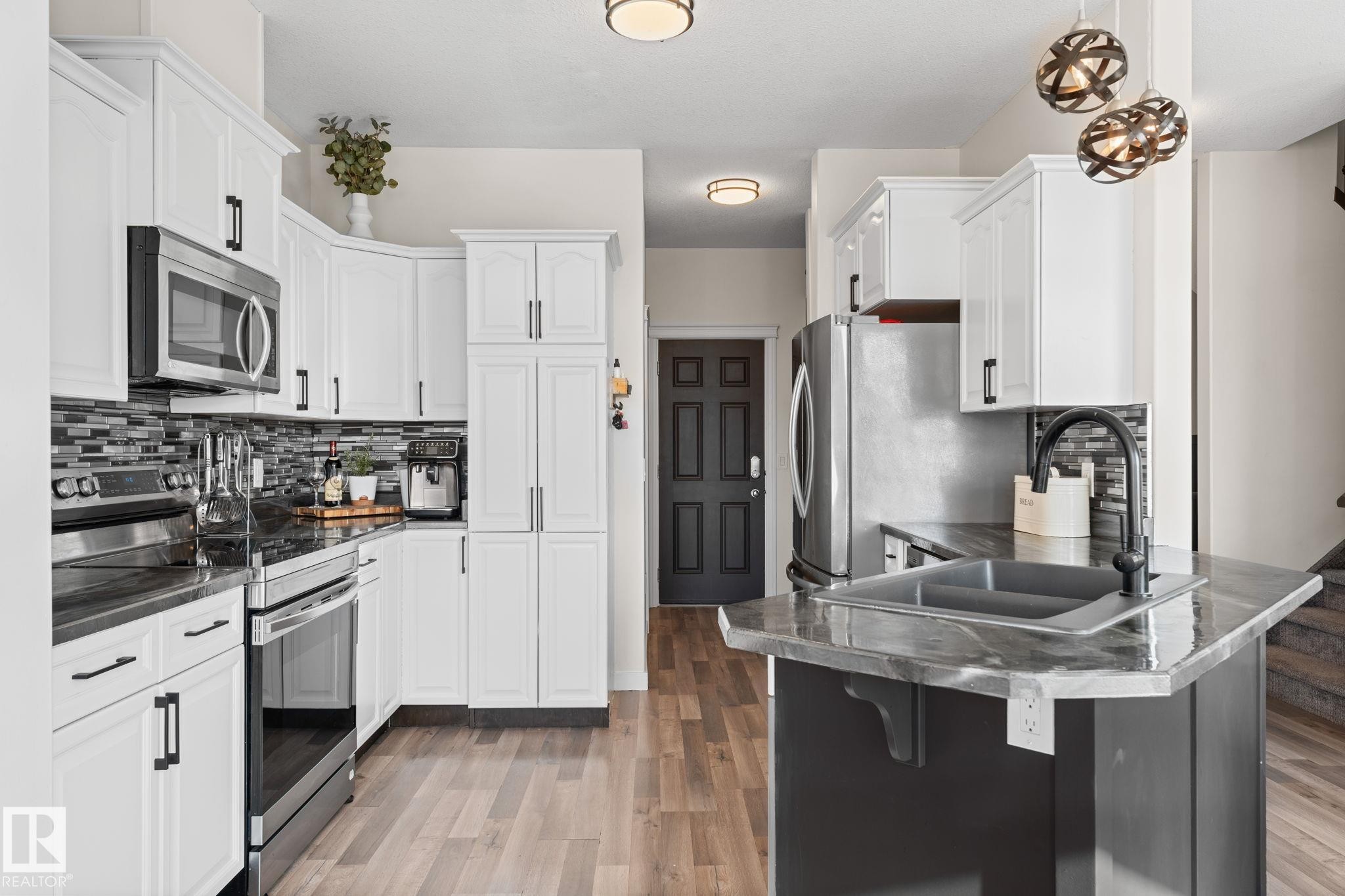 Contemporary kitchen featuring white cabinetry, stainless steel appliances, dark countertops, and wood-finish flooring - #5 4900 62 St, Beaumont, AB