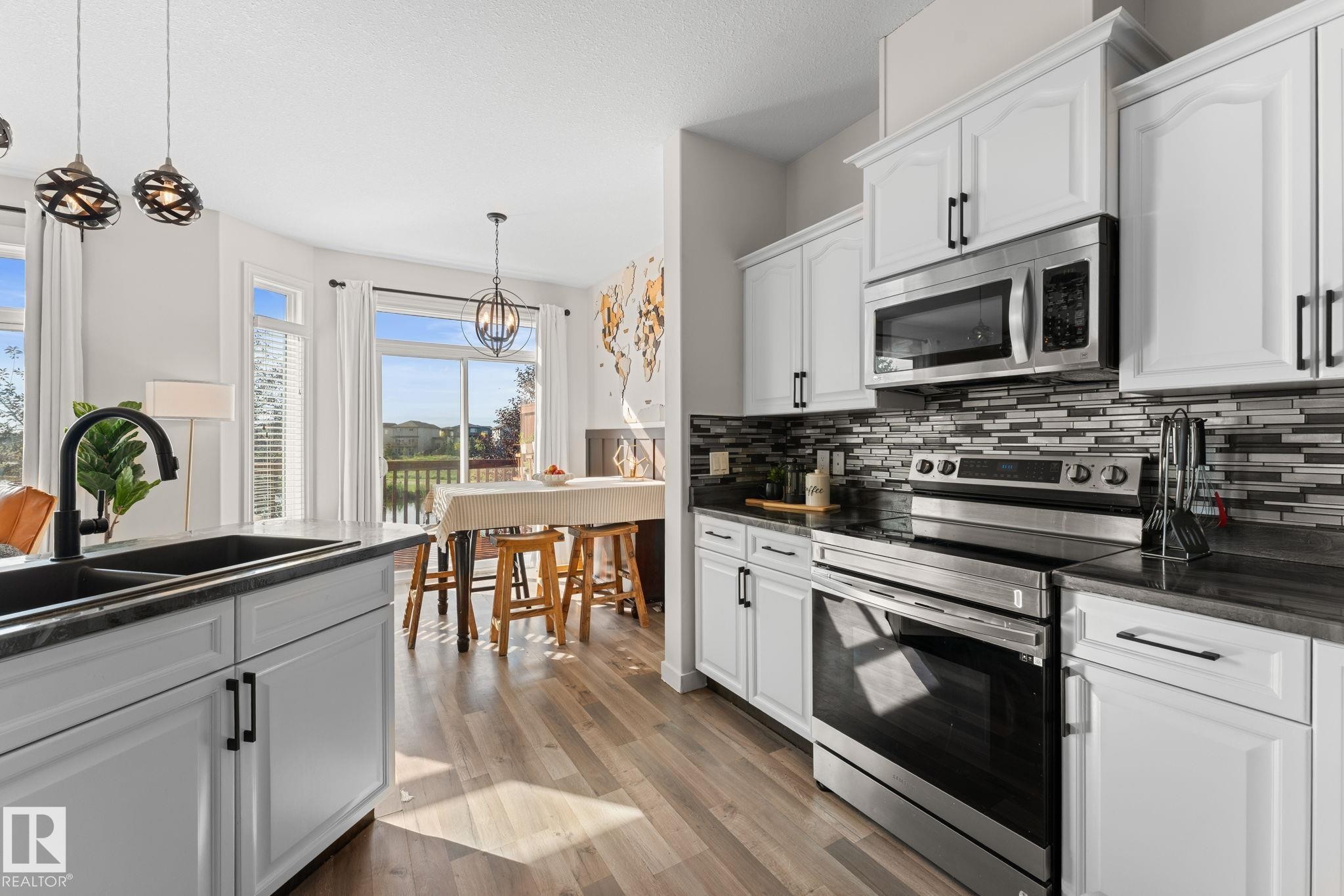 White cabinetry with black hardware, stainless steel appliances, dark countertops, a tiled backsplash, and wood-finish flooring - #5 4900 62 St, Beaumont, AB