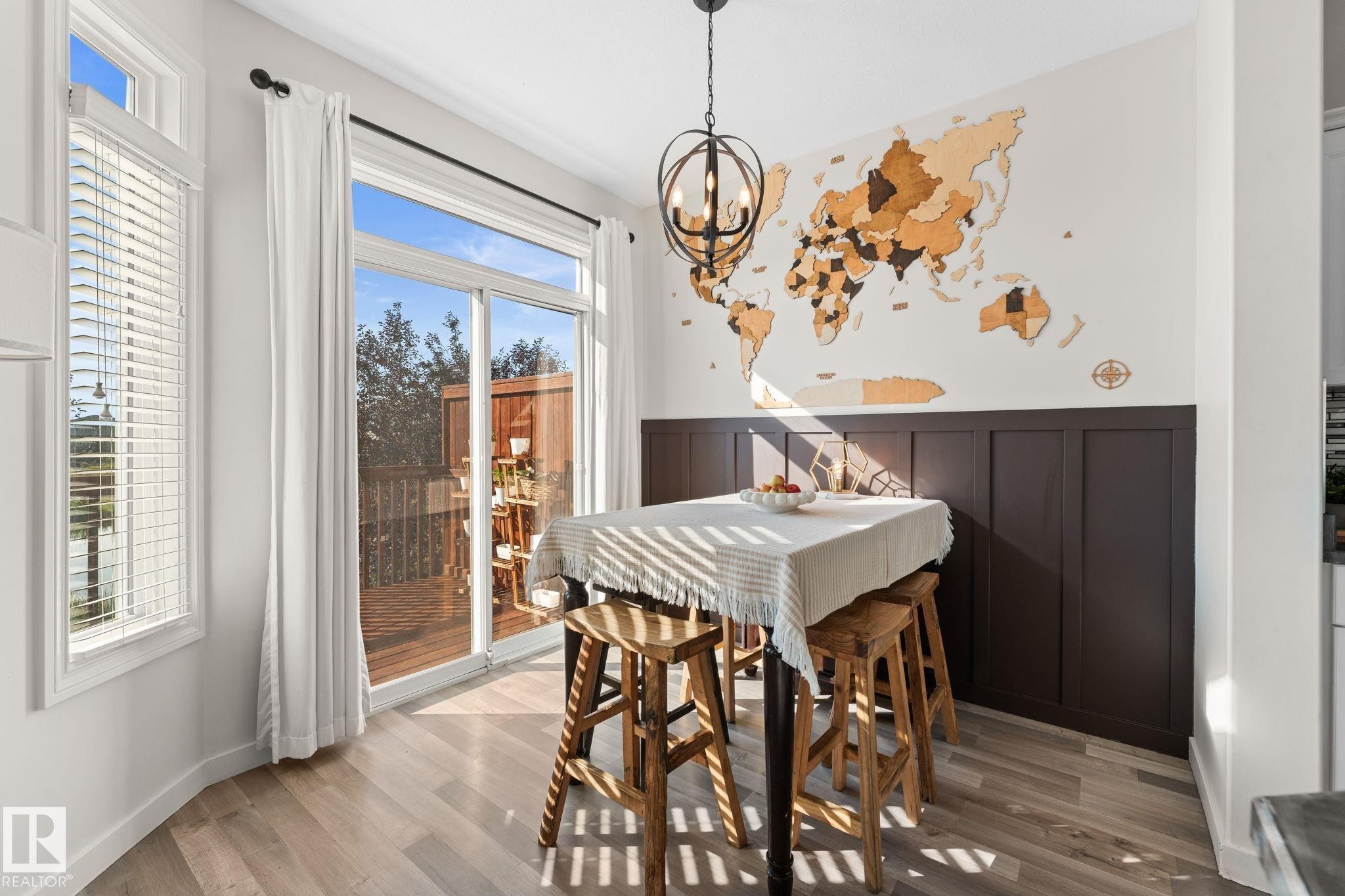 Wood-finish flooring, sliding glass doors to exterior, dark wainscoting, and a decorative orb chandelier - #5 4900 62 St, Beaumont, AB