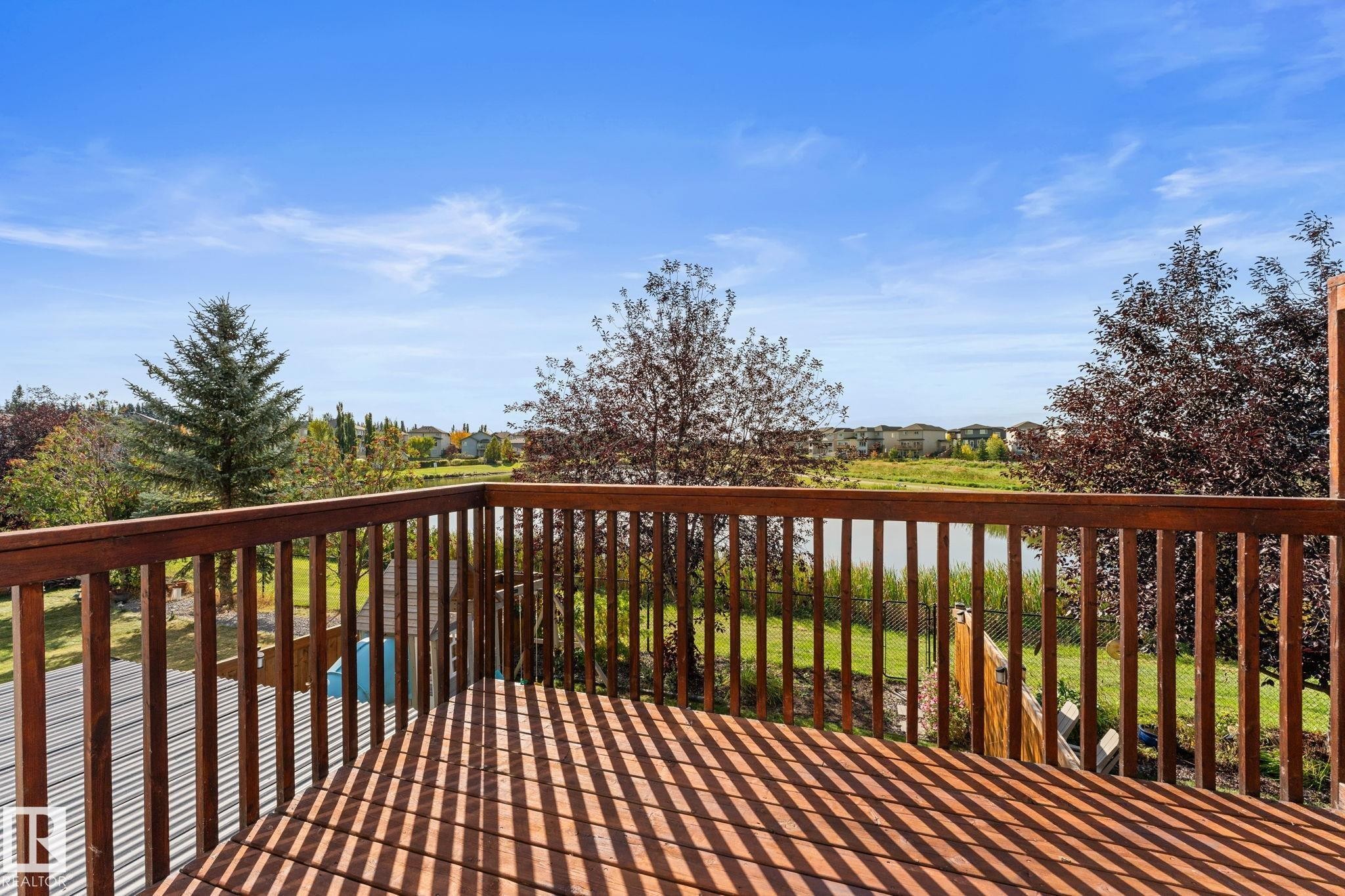 Wood-finish deck with a wood railing, offering a waterfront backdrop - #5 4900 62 St, Beaumont, AB