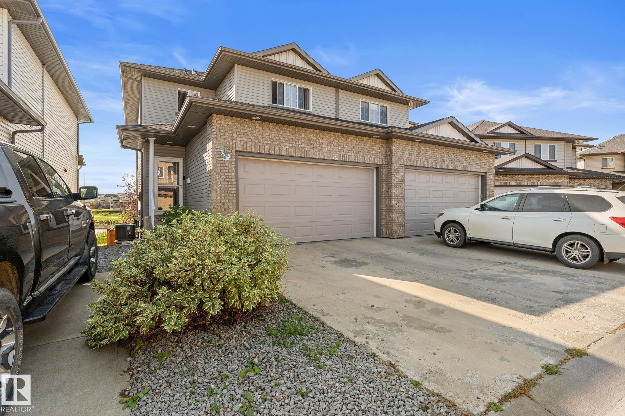 Exterior featuring brick and siding finishes, two attached garage doors, concrete driveway, and established landscaping - #5 4900 62 St, Beaumont, AB
