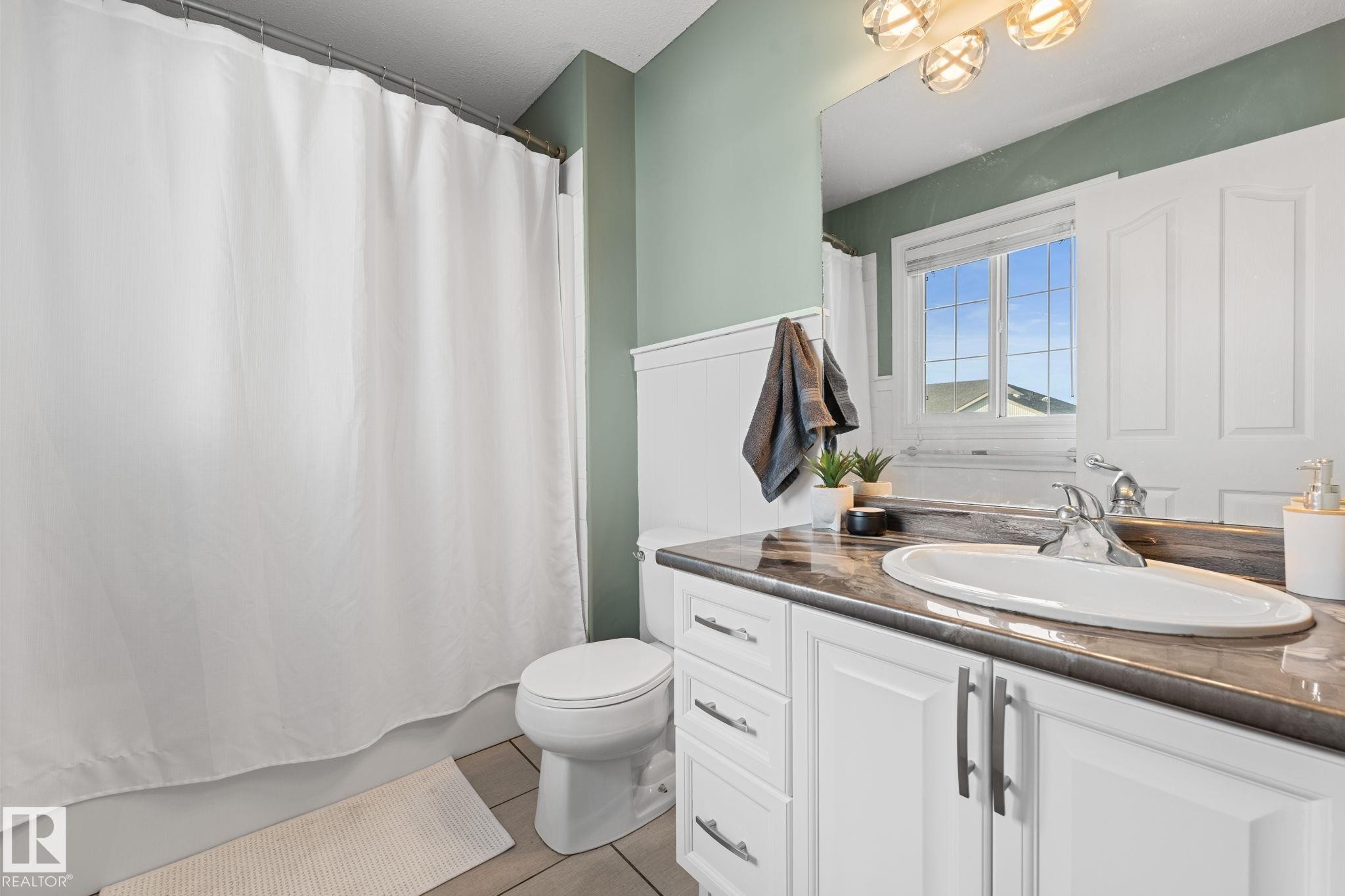 White vanity with integrated sink and chrome faucet, dark countertop, and decorative wall paneling - #5 4900 62 St, Beaumont, AB