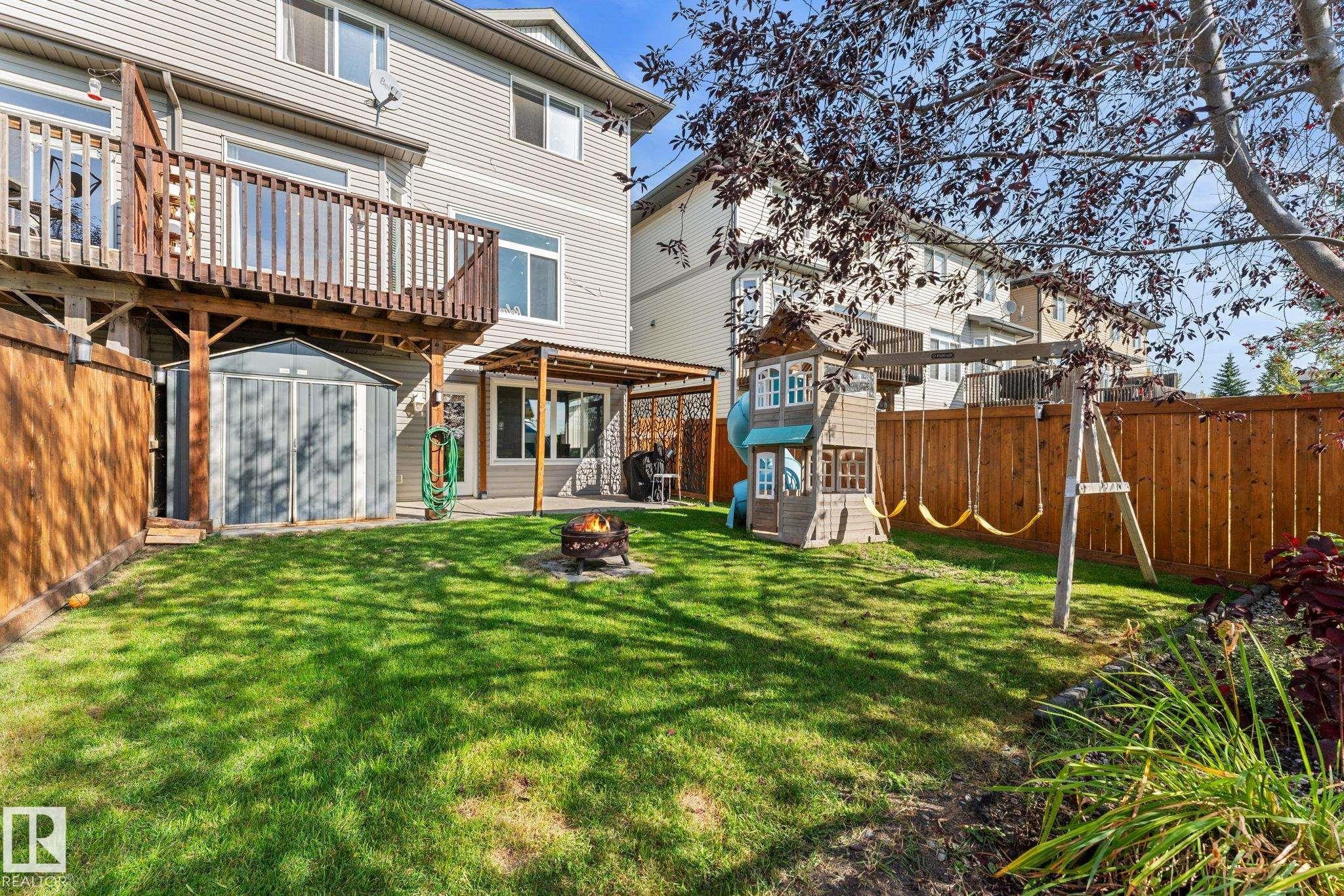 Expansive backyard featuring a manicured lawn, wood fencing, a ground-level patio with a pergola, and a raised wood-finish deck - #5 4900 62 St, Beaumont, AB