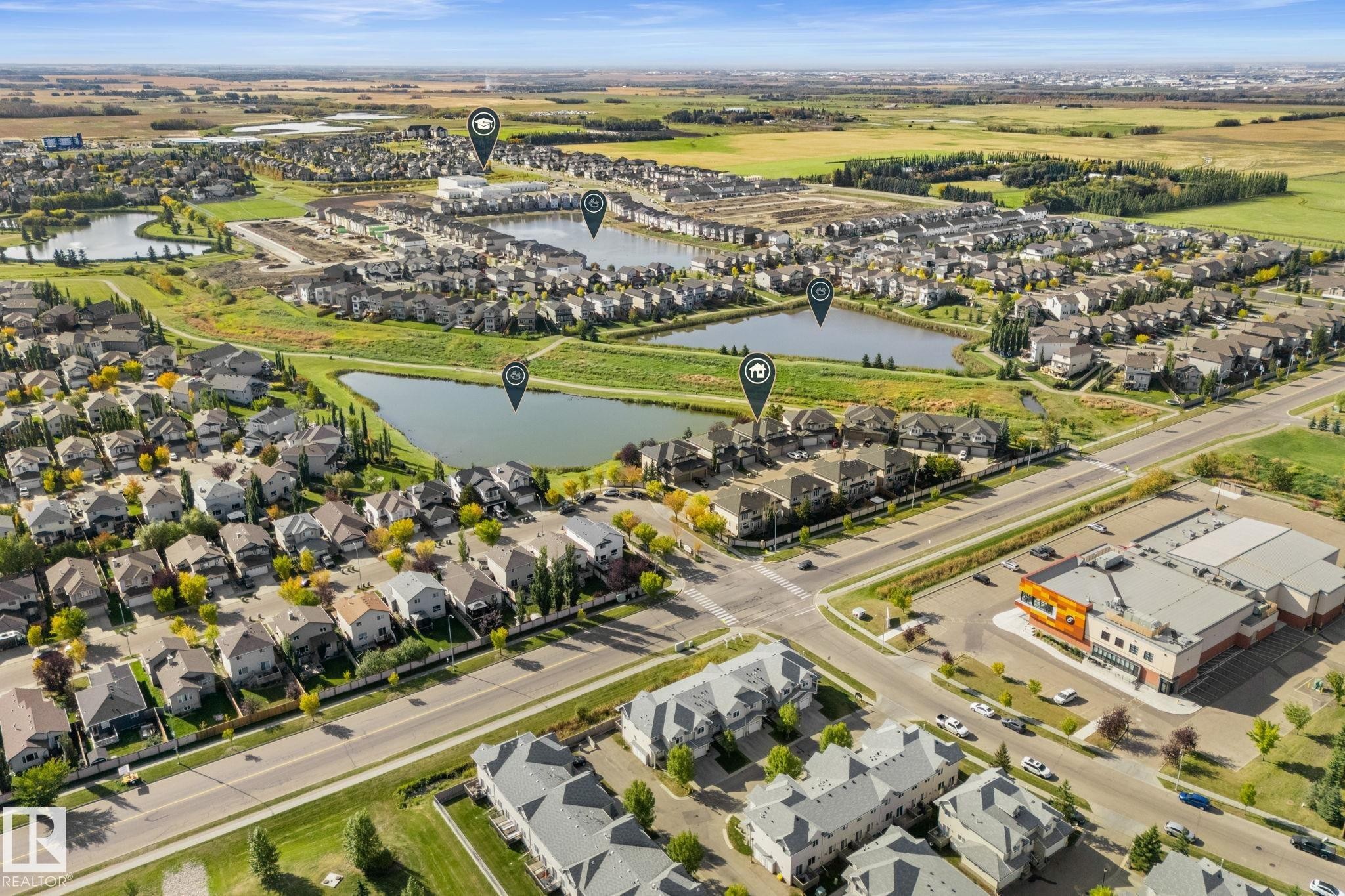 Aerial perspective of a residential community with multiple water features, established roadways, and commercial buildings - #5 4900 62 St, Beaumont, AB