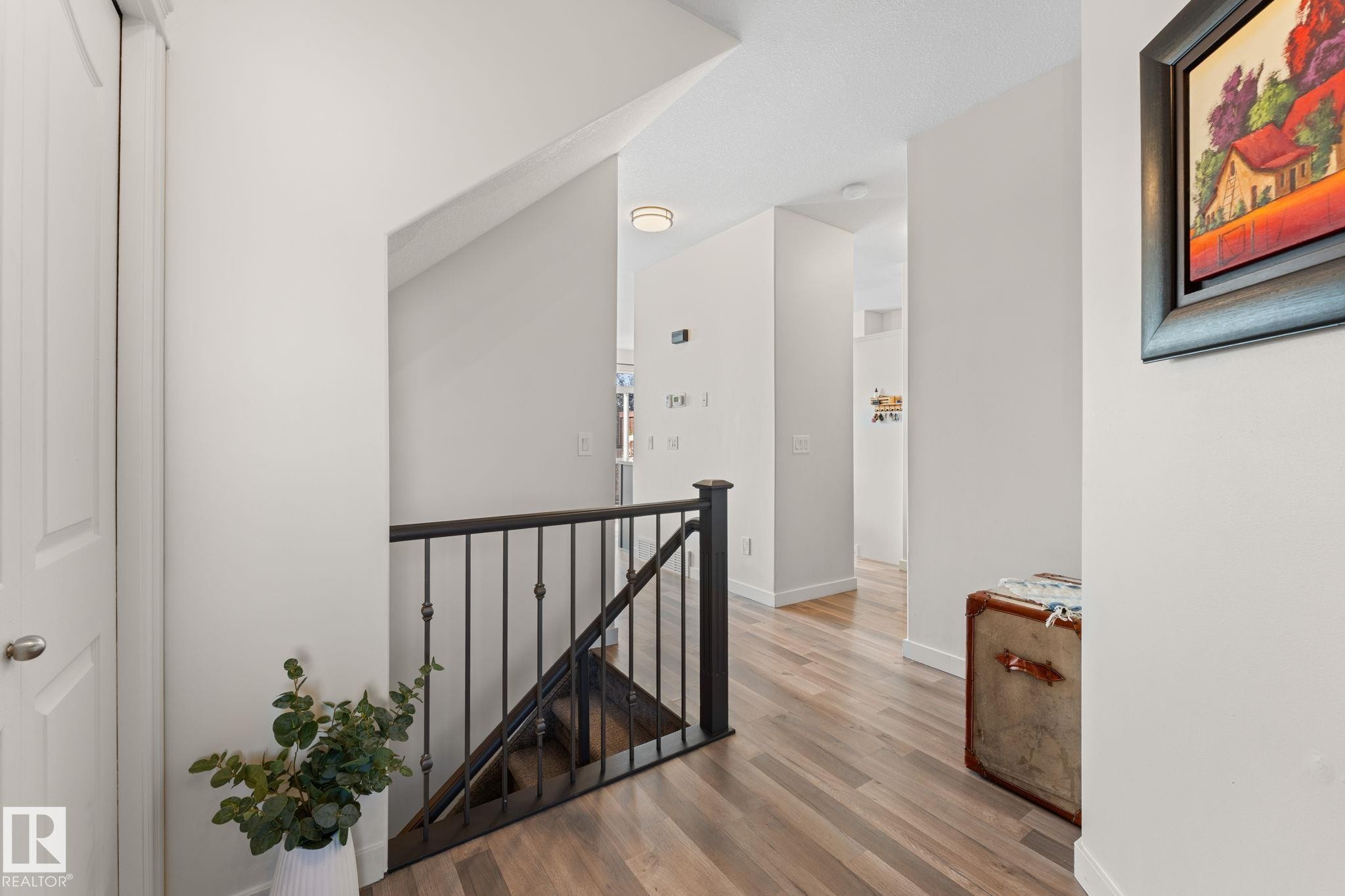 Wood-finish flooring throughout, featuring a staircase with black metal balusters and a dark wood handrail - #5 4900 62 St, Beaumont, AB