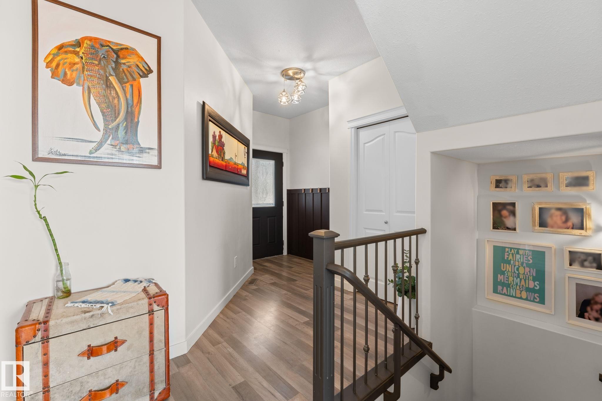 Wood-finish flooring, white walls, and a staircase with dark wood handrails and wrought iron balusters - #5 4900 62 St, Beaumont, AB