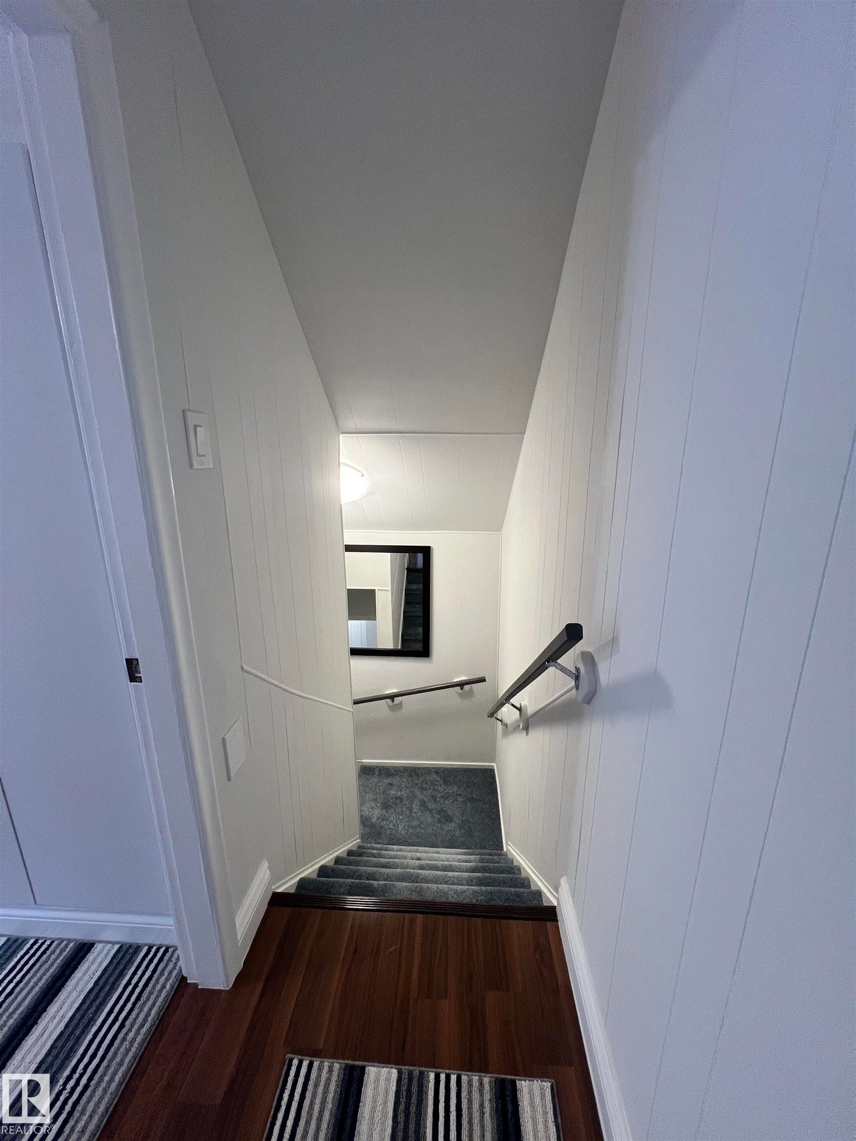 Rich wood-finish flooring transitioning to carpeted stairs with a handrail - 11908 131 Street Nw, Edmonton, AB