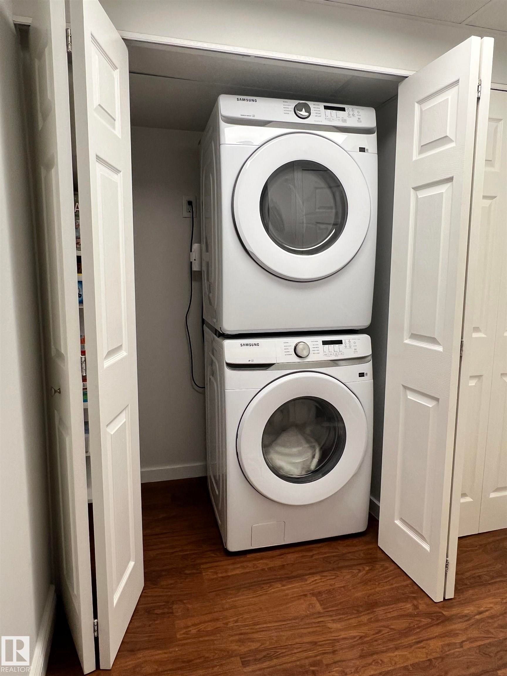 Built-in laundry closet with bi-fold doors, stacked white appliances, and wood-finish flooring - 11908 131 Street Nw, Edmonton, AB