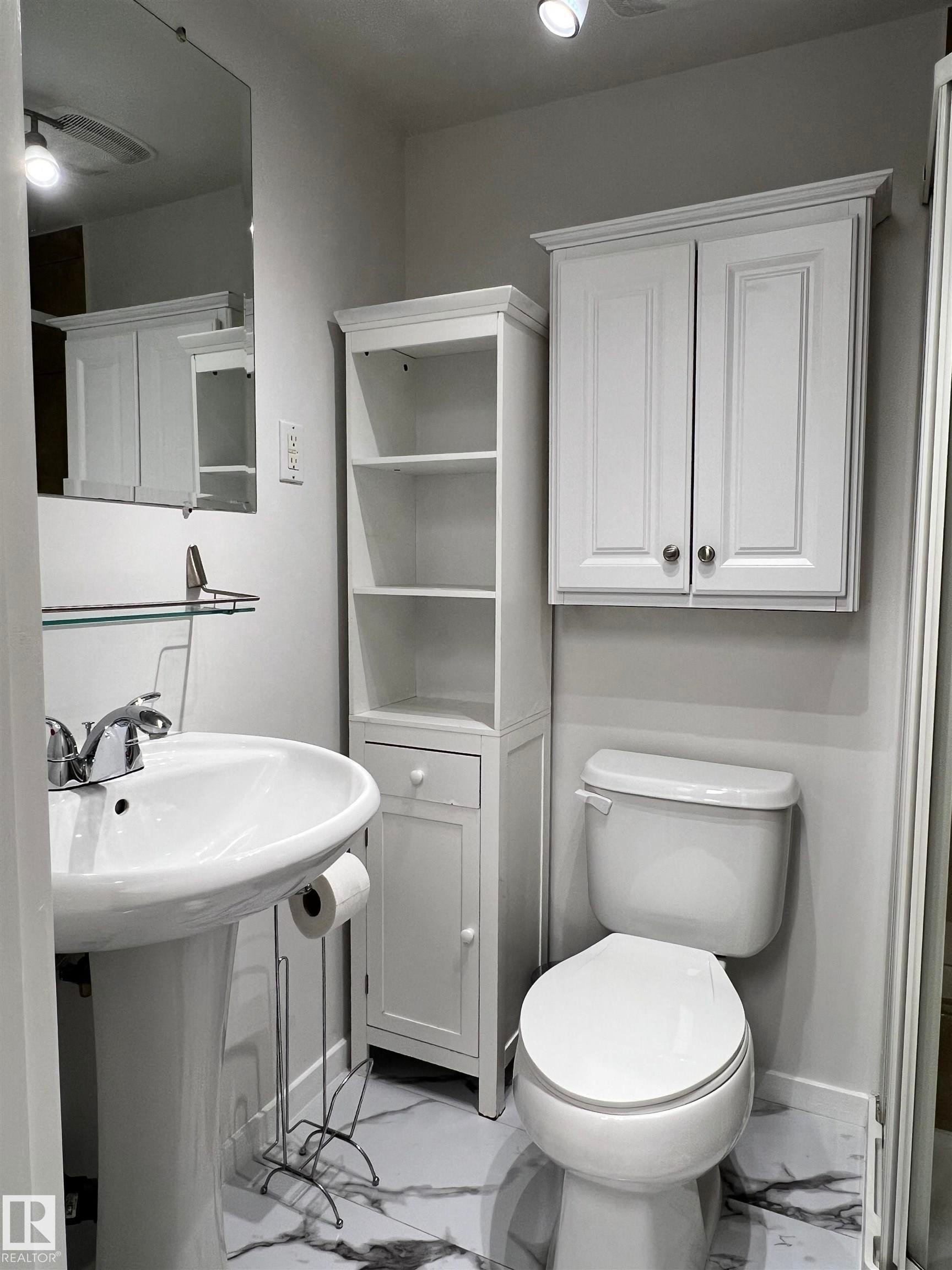 Pedestal sink with chrome-finish faucet, white toilet, white wall-mounted cabinet, and built-in shelving unit - 11908 131 Street Nw, Edmonton, AB