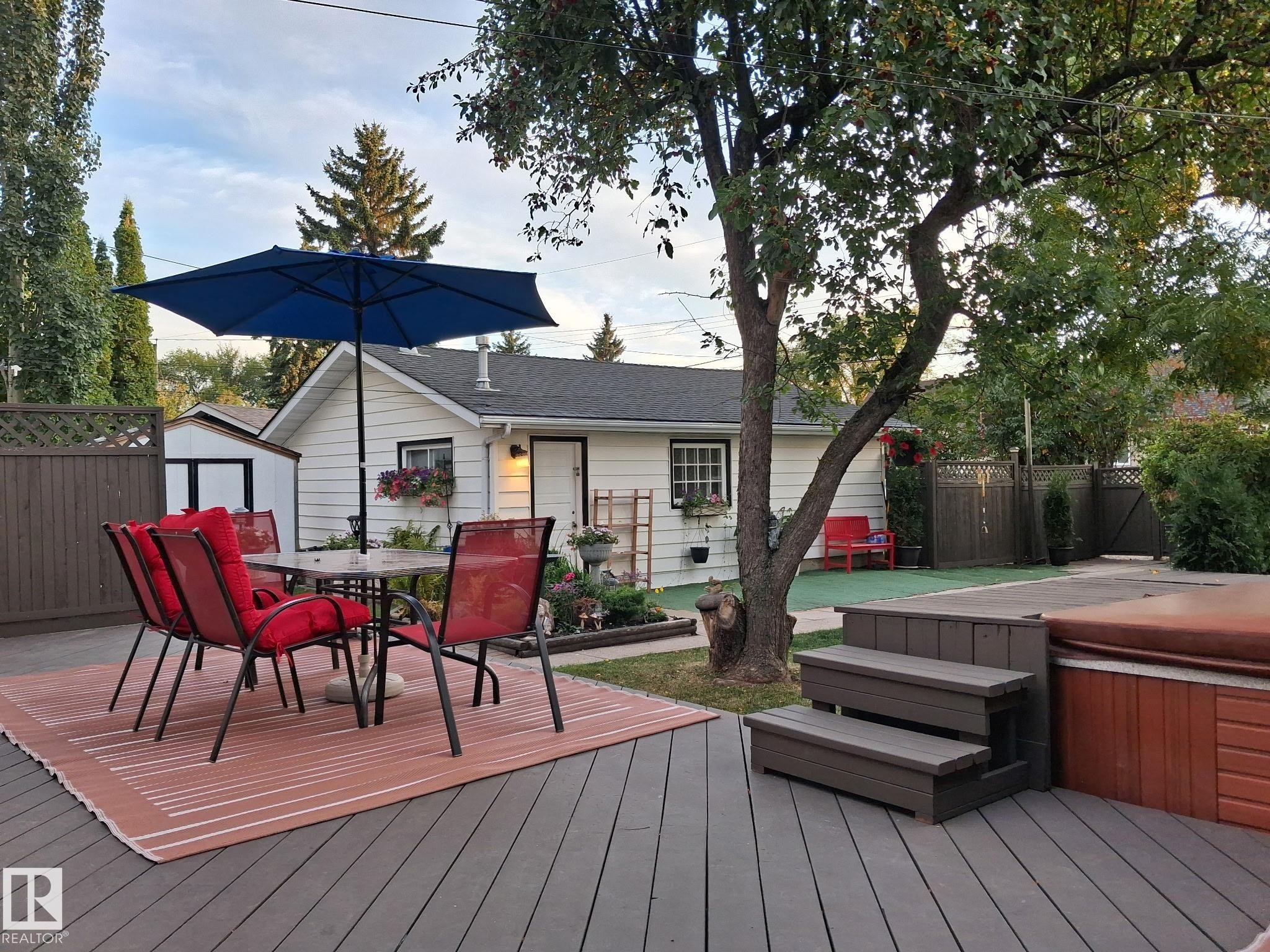 Expansive outdoor deck with a built-in hot tub, privacy fencing, mature trees, and a detached structure - 11908 131 Street Nw, Edmonton, AB