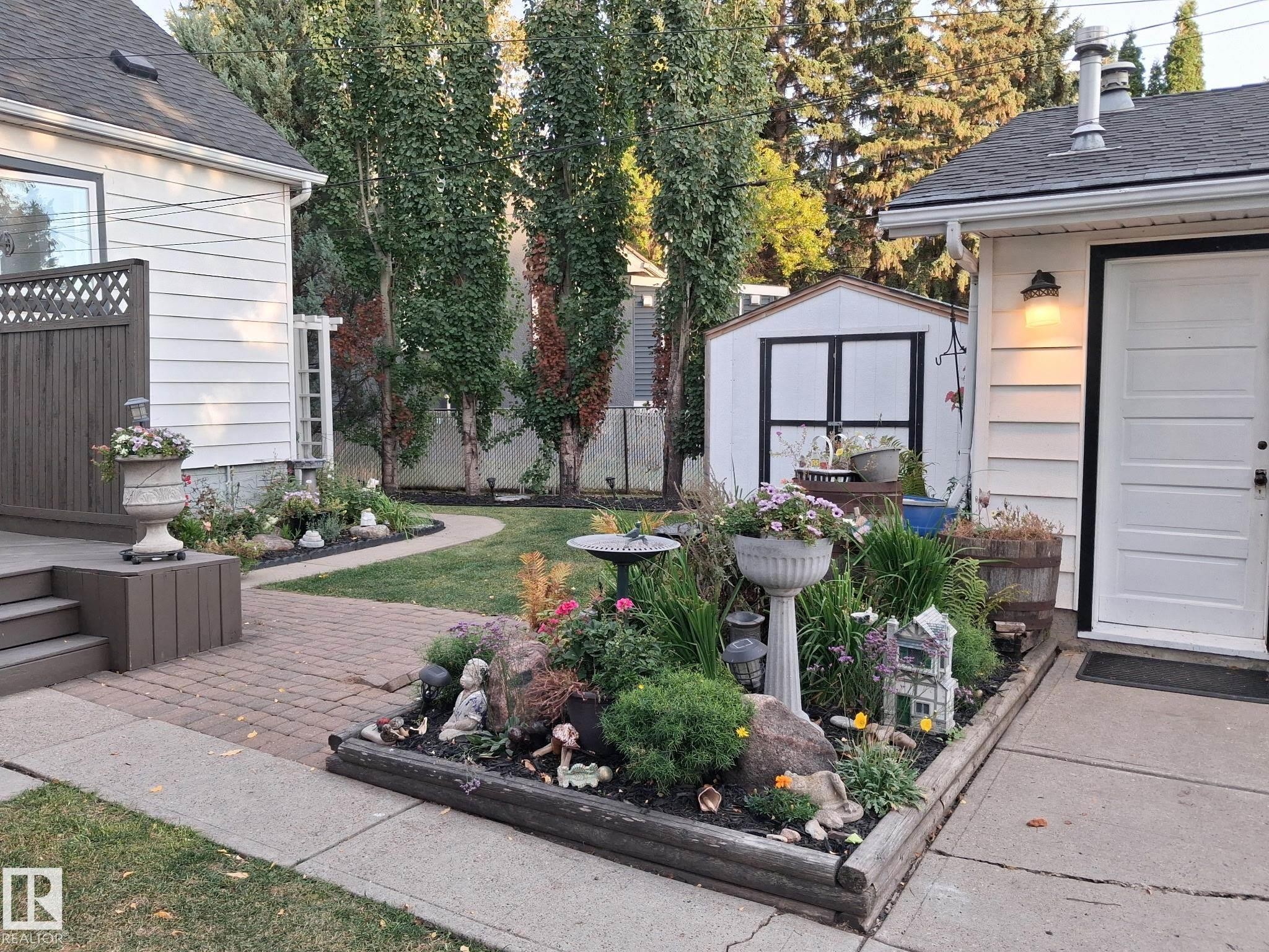 Private backyard featuring an elevated wood deck, brick paver patio, a manicured lawn, and a storage shed - 11908 131 Street Nw, Edmonton, AB