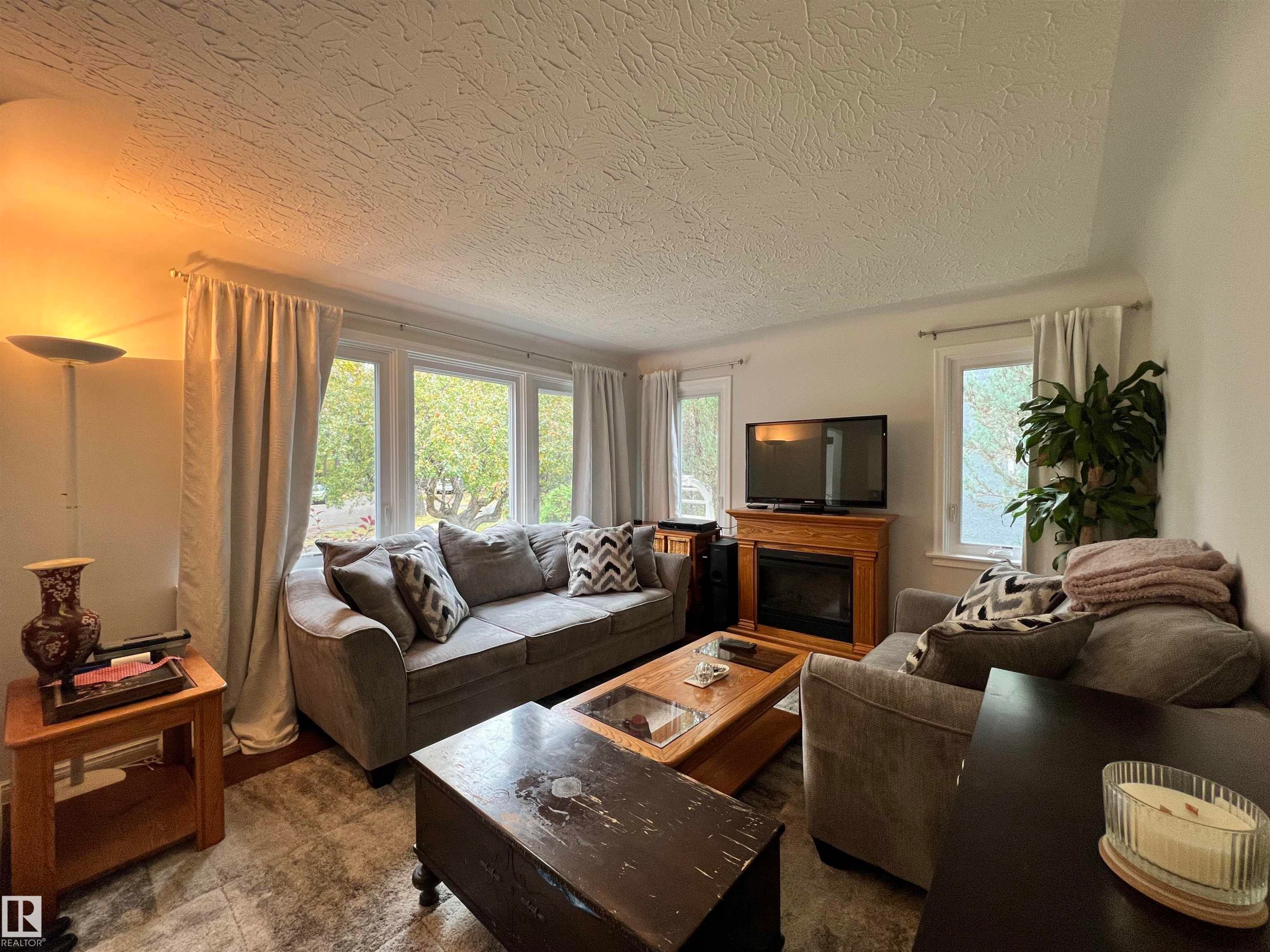 Living area featuring a fireplace with a wood surround, large window, and tiled flooring - 11908 131 Street Nw, Edmonton, AB