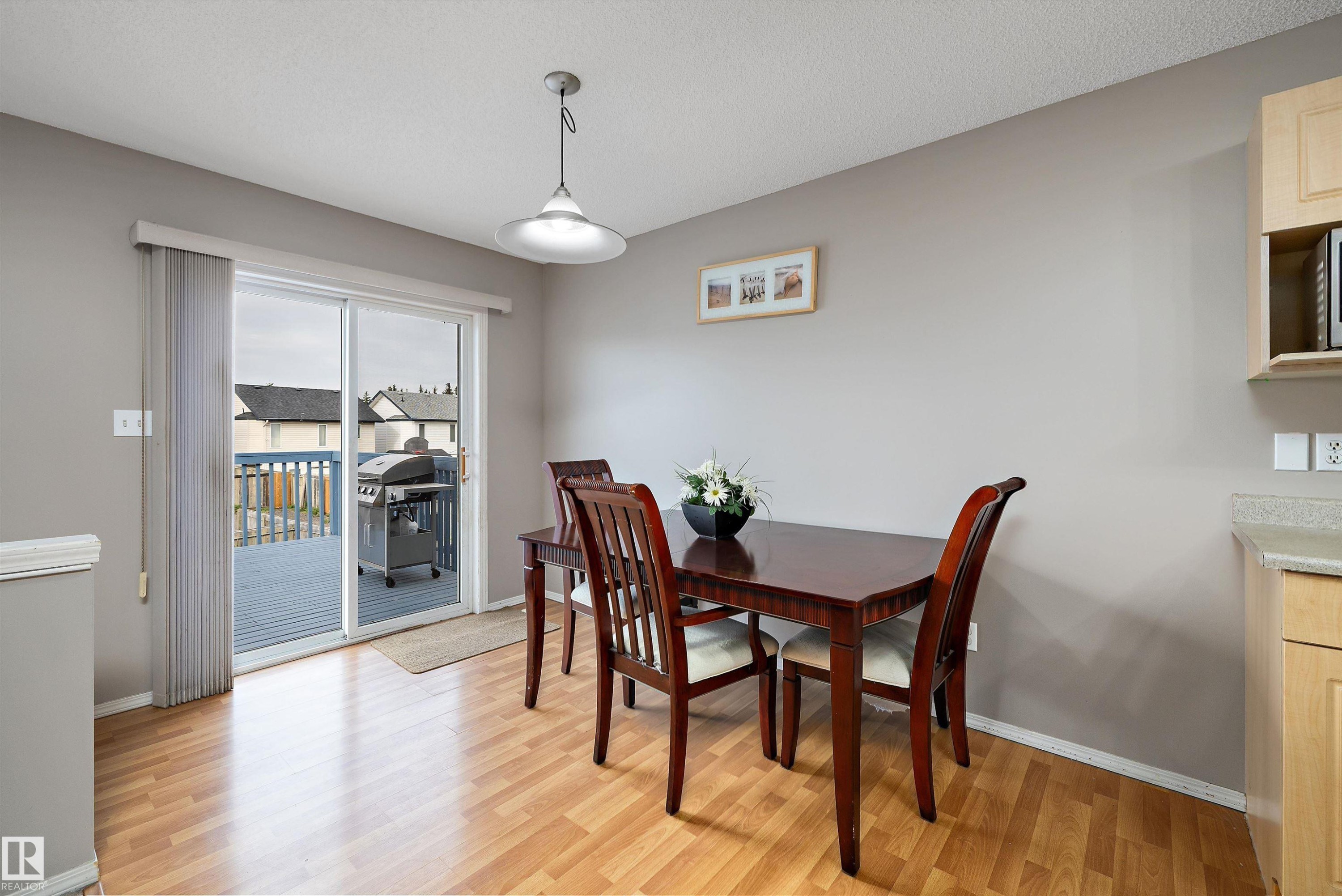 Sliding glass door leading to an outdoor deck, wood-finish flooring, overhead pendant light, light wood cabinetry, and a light-toned countertop - 3114 32 Avenue Nw, Edmonton, AB