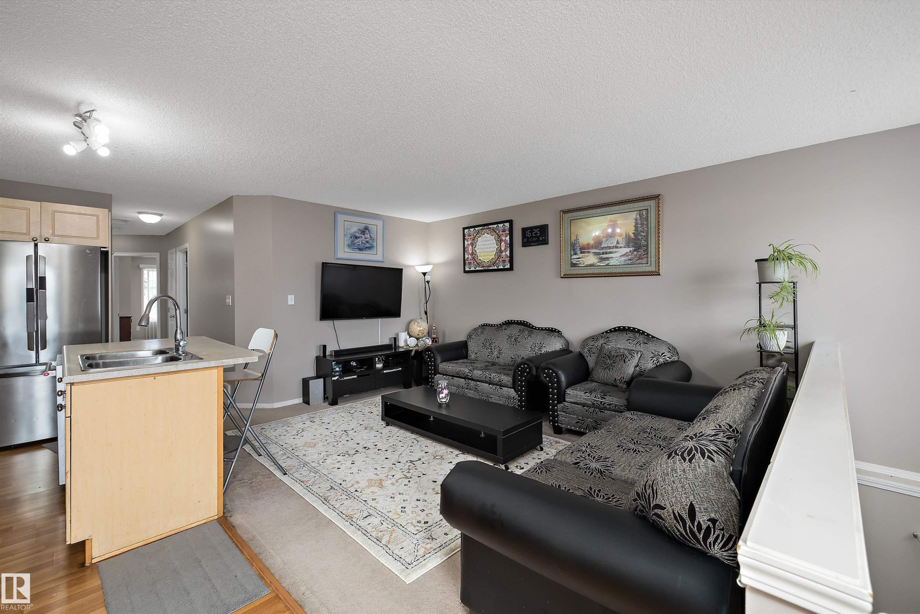 Open-concept living area with a kitchen island featuring an integrated sink, stainless steel appliances, and wood-finish flooring - 3114 32 Avenue Nw, Edmonton, AB