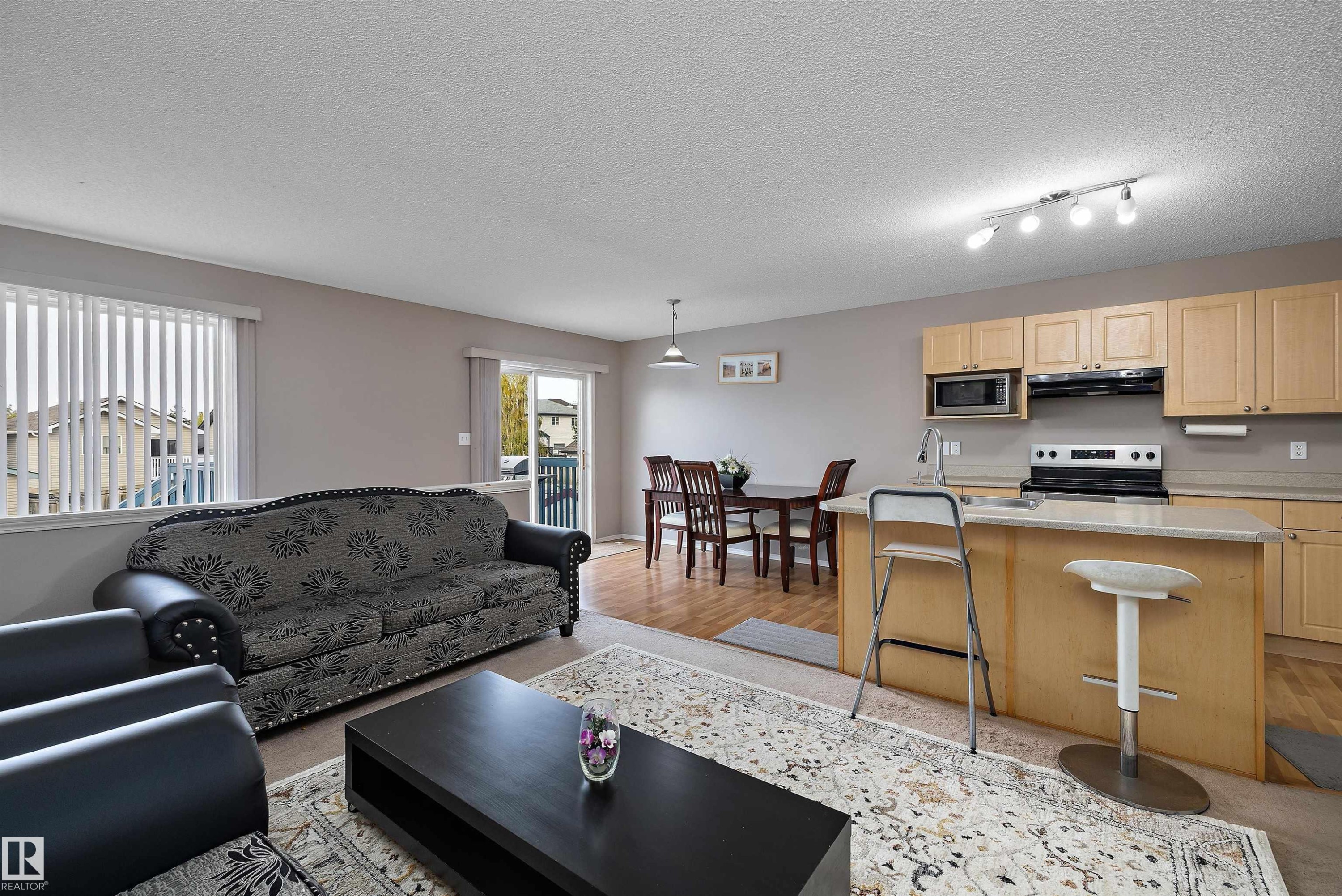 Open-concept living space featuring a kitchen island, wood-finish flooring, light wood cabinetry, and a sliding glass door - 3114 32 Avenue Nw, Edmonton, AB