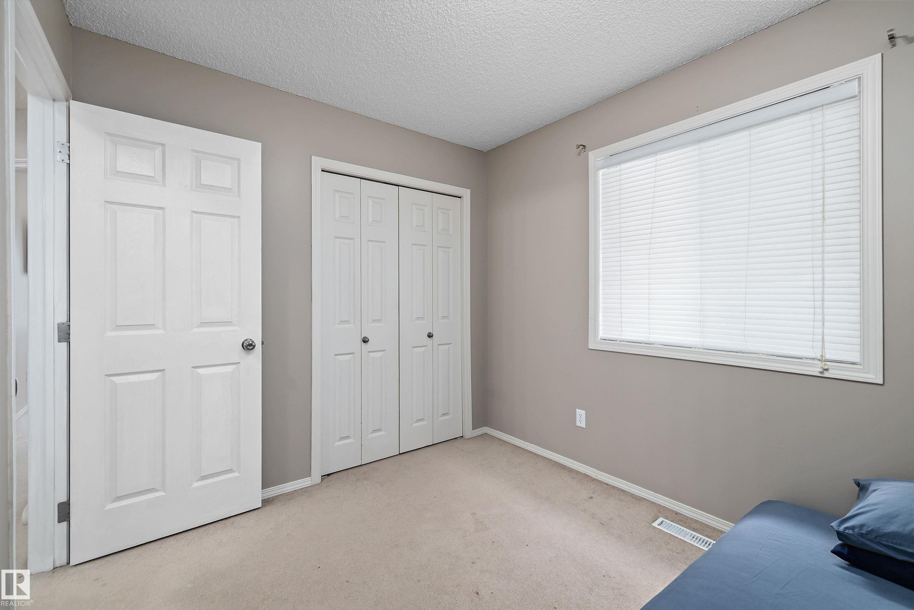 Neutral wall paint with carpet flooring, featuring a large window with blinds, and white bi-fold closet doors - 3114 32 Avenue Nw, Edmonton, AB